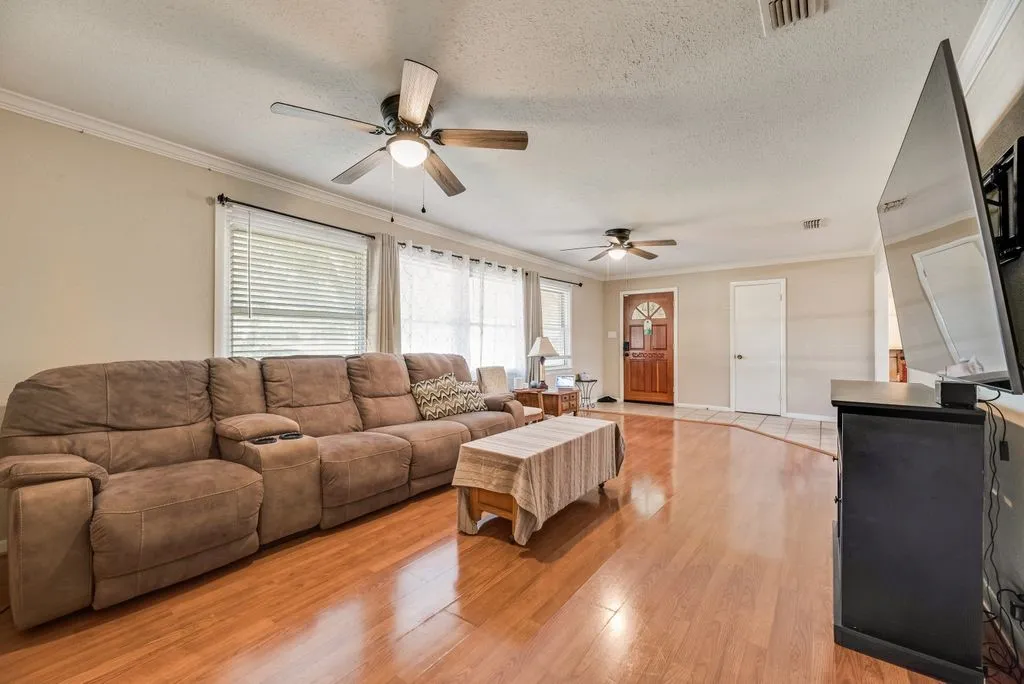 Wood-finish flooring, multiple windows with blinds, two ceiling fans with integrated lighting, and crown molding