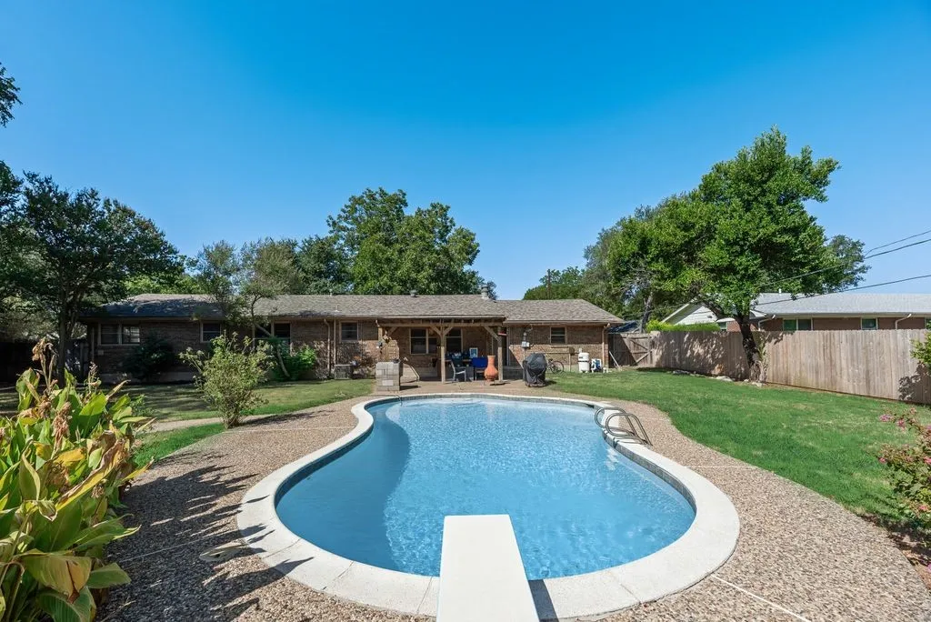 Freeform swimming pool with a diving board, surrounded by exposed aggregate concrete decking, and a covered patio area