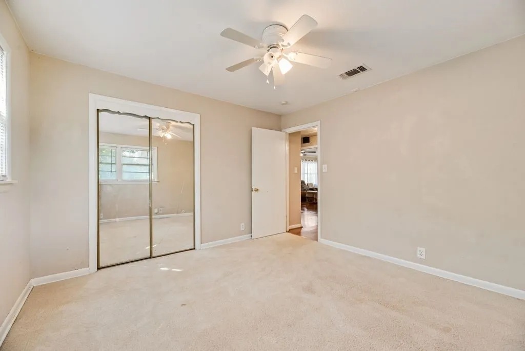 Neutral tone walls with an overhead ceiling fan light fixture, carpeted flooring, and a mirrored closet door