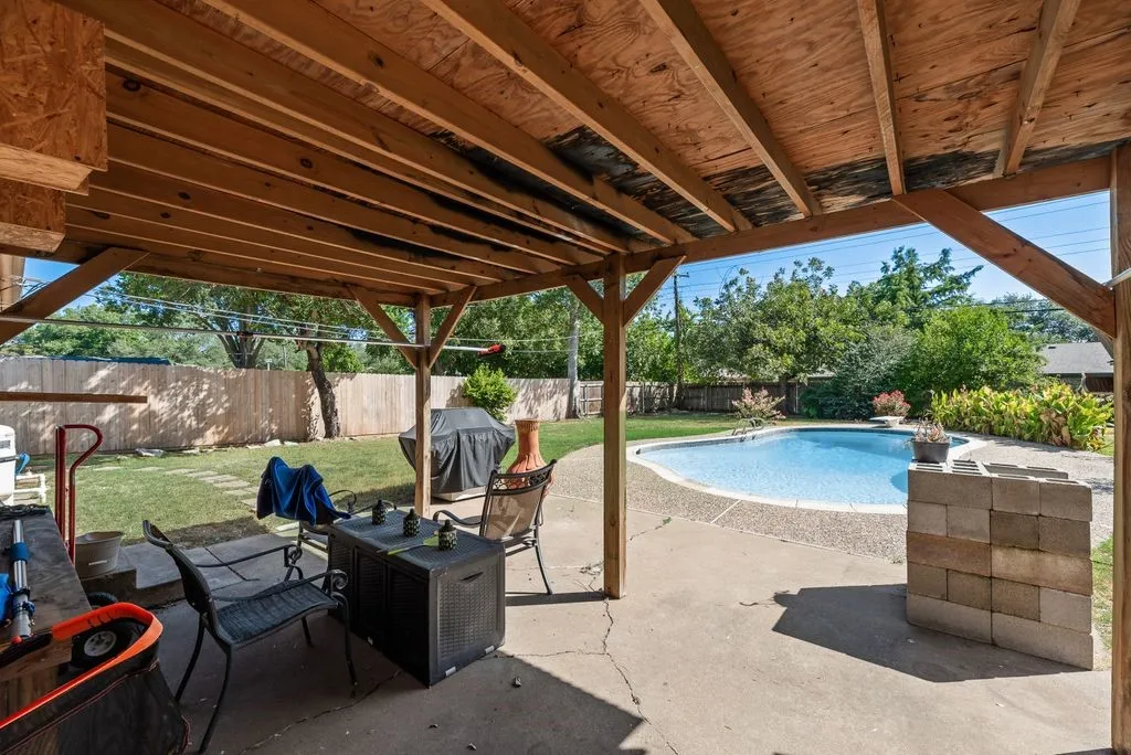 Expansive backyard featuring a concrete patio, wood-framed covered area, and a fenced perimeter