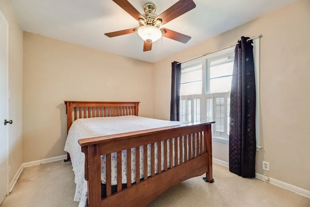 Plush carpet flooring, ceiling fan with integrated lighting, and multiple windows with plantation shutters