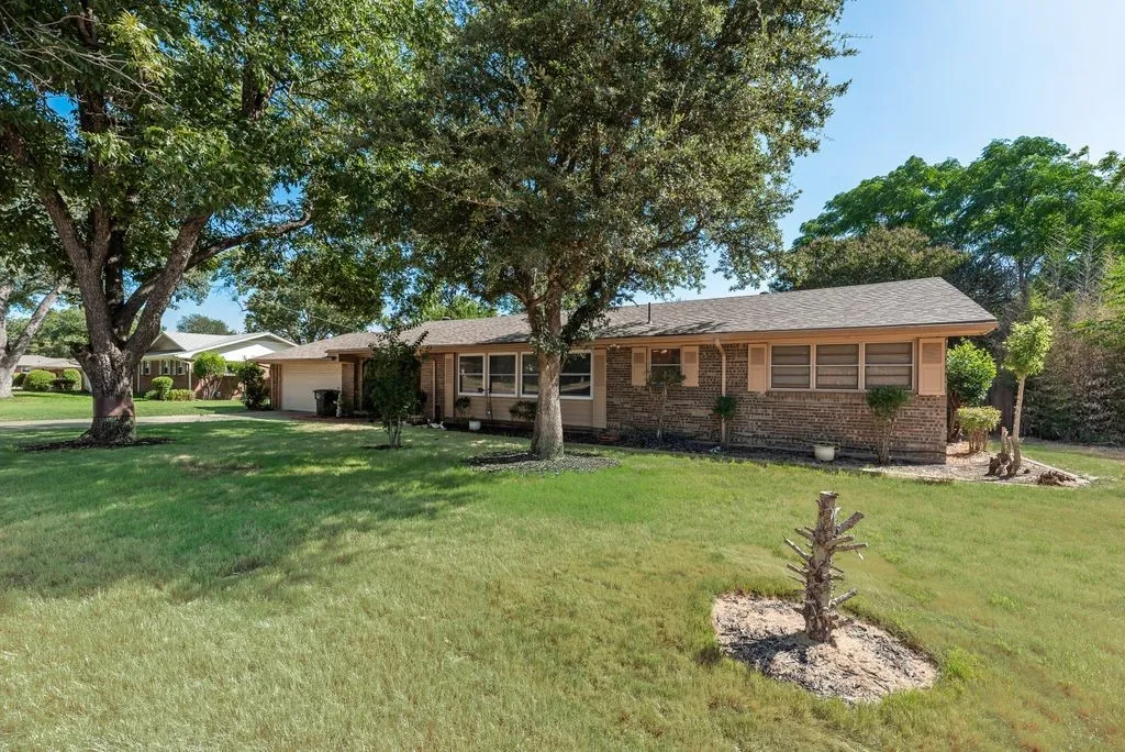 Brick exterior with a shingle roof and mature trees on a grassy lawn