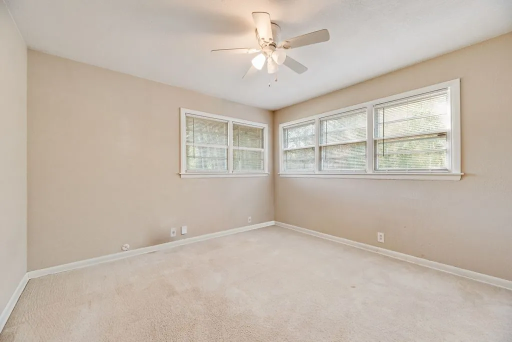 Neutral-toned walls, light-colored carpeting, multiple windows, and a ceiling fan with integrated lighting