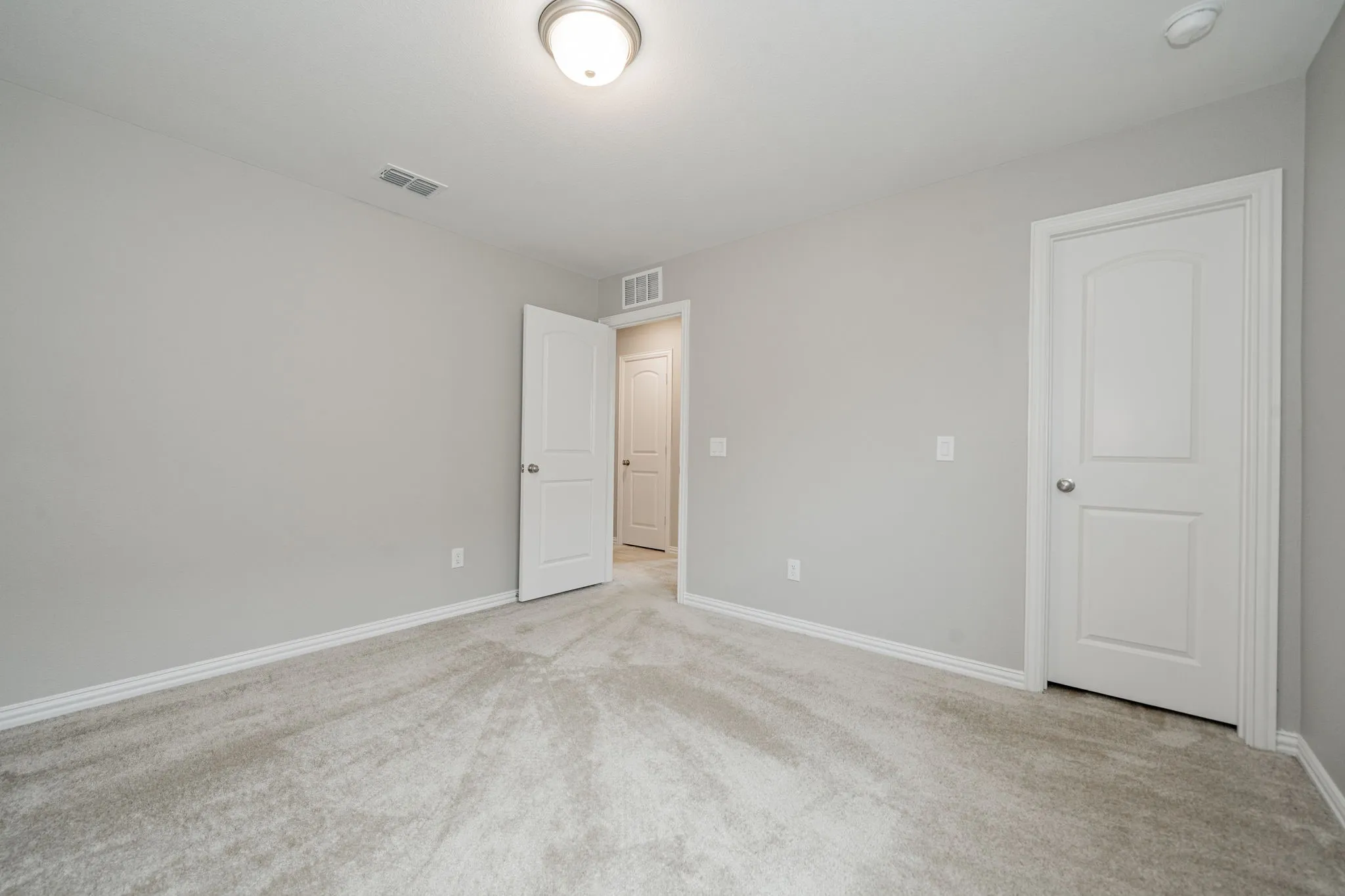 Light gray walls, light gray carpeting, flush mount ceiling light fixture, white interior doors, and white baseboards