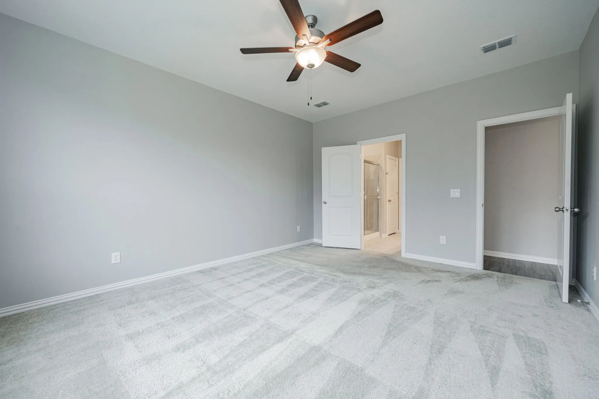 Spacious bedroom featuring neutral gray walls, recessed lighting, and a ceiling fan with integrated light fixture