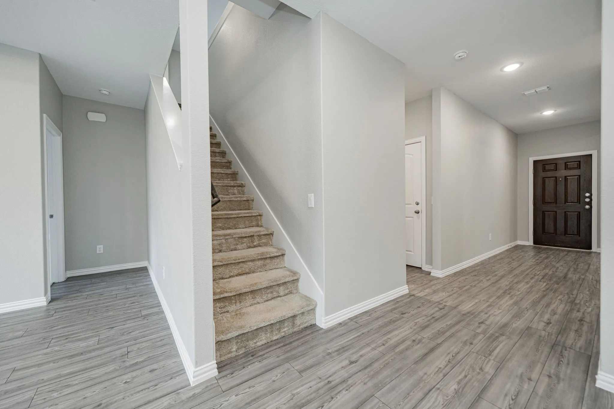 Wood-finish flooring, recessed lighting, carpeted staircase, and a paneled entry door
