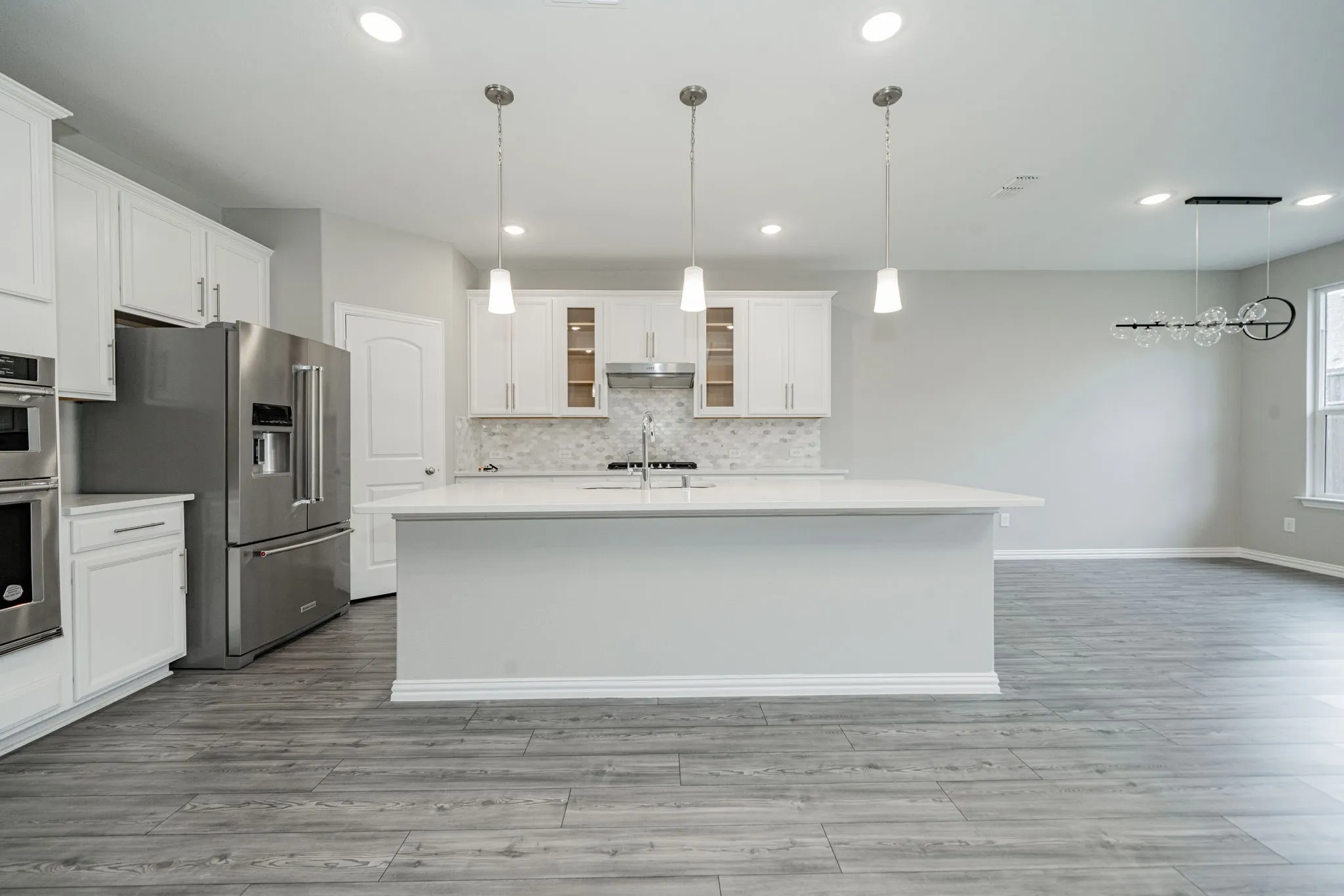Open concept kitchen featuring an expansive center island, white cabinetry, stainless steel appliances, and wood-finish flooring