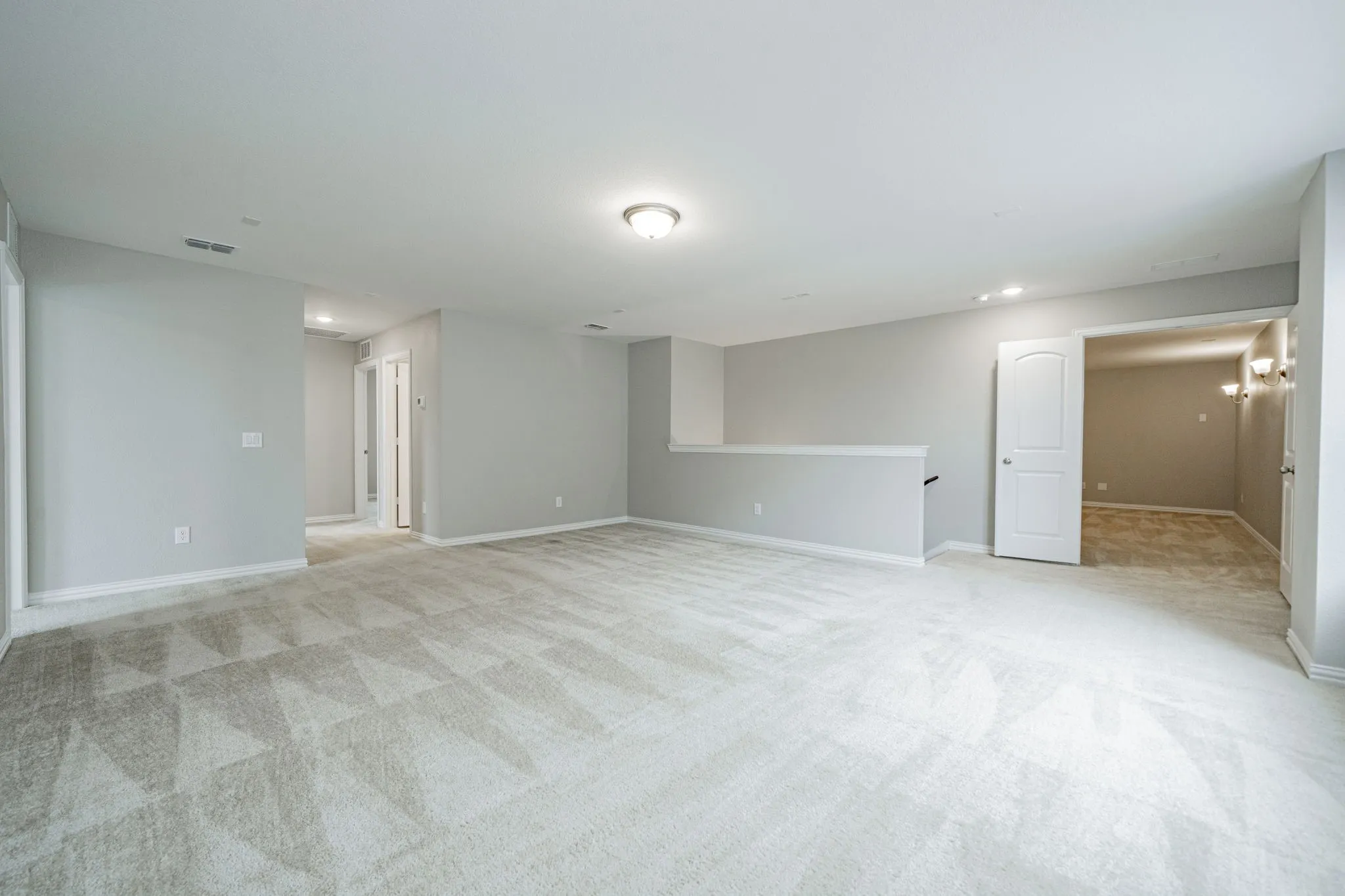 Spacious room with patterned carpet flooring, light gray wall paint, and overhead lighting