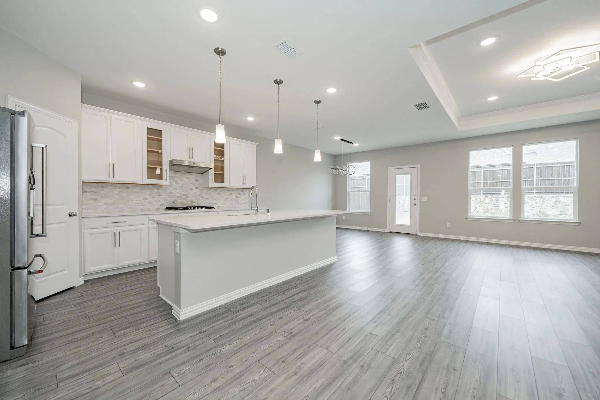Open-concept living space with wood-finish flooring, a kitchen island, white cabinetry, a decorative coffered ceiling, and pendant lighting