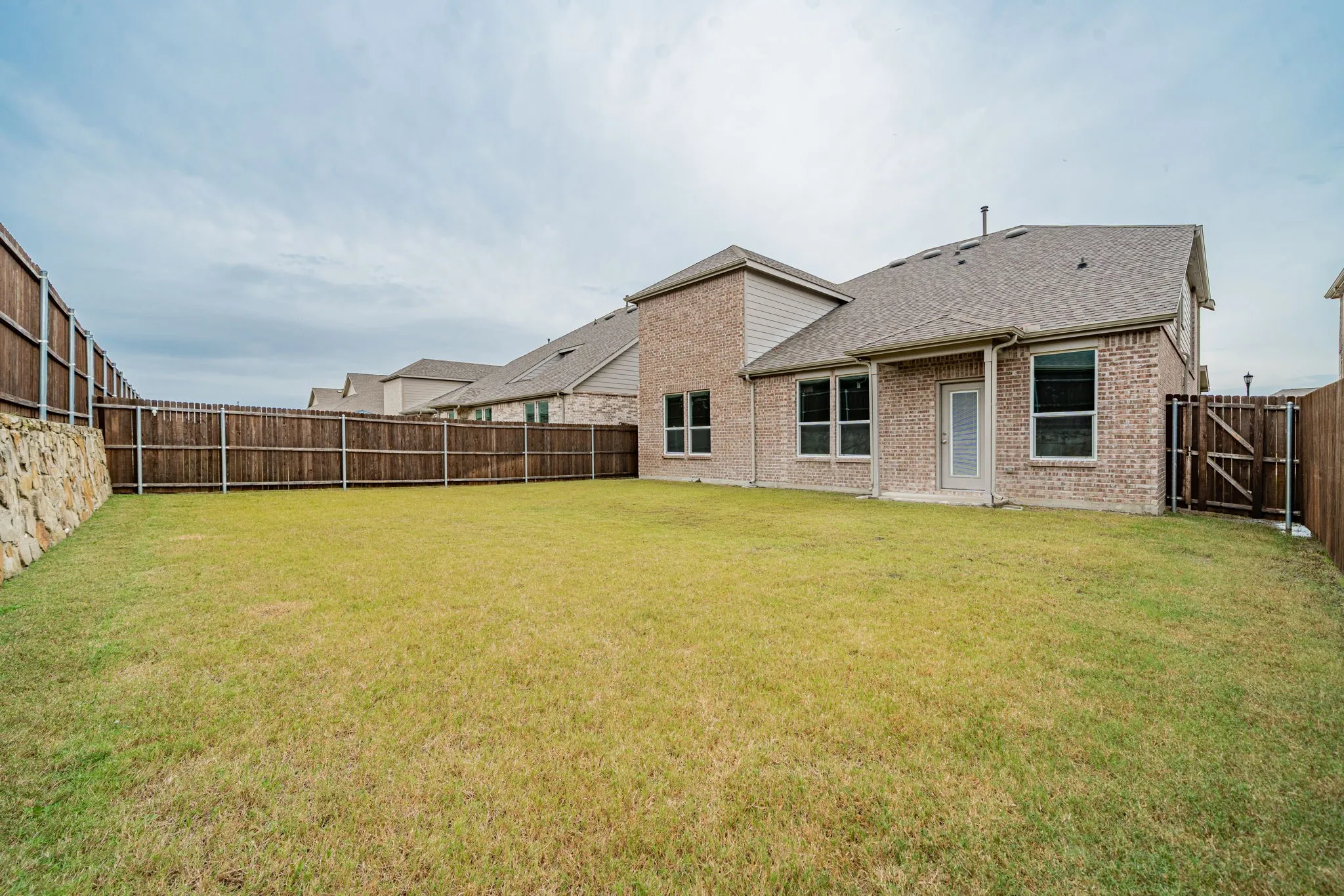 Expansive backyard featuring a manicured lawn, full privacy fencing, and a stone retaining wall