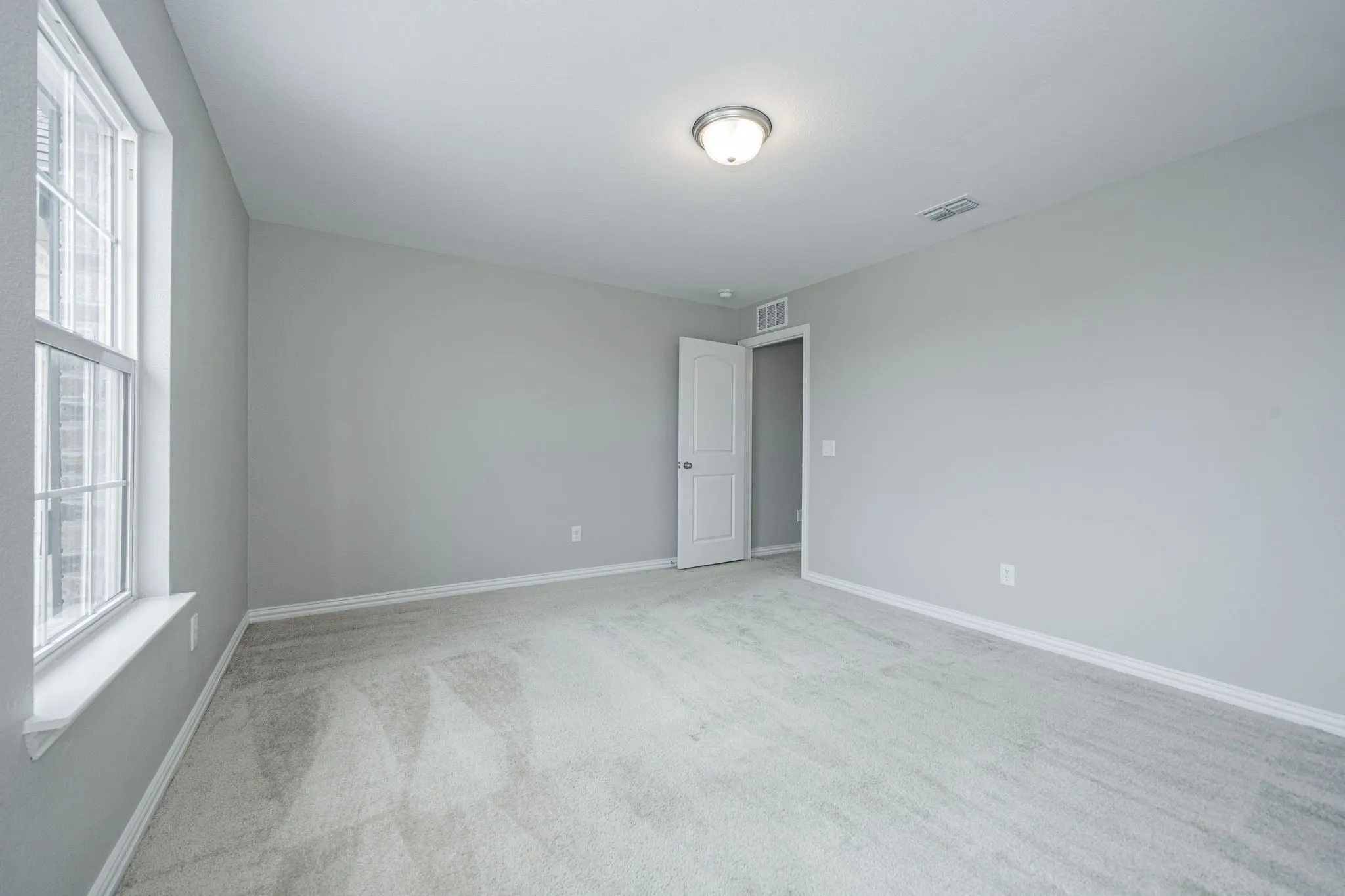 Expansive room featuring light gray carpeting, neutral wall color, a double-paned window, and a flush-mount ceiling light fixture