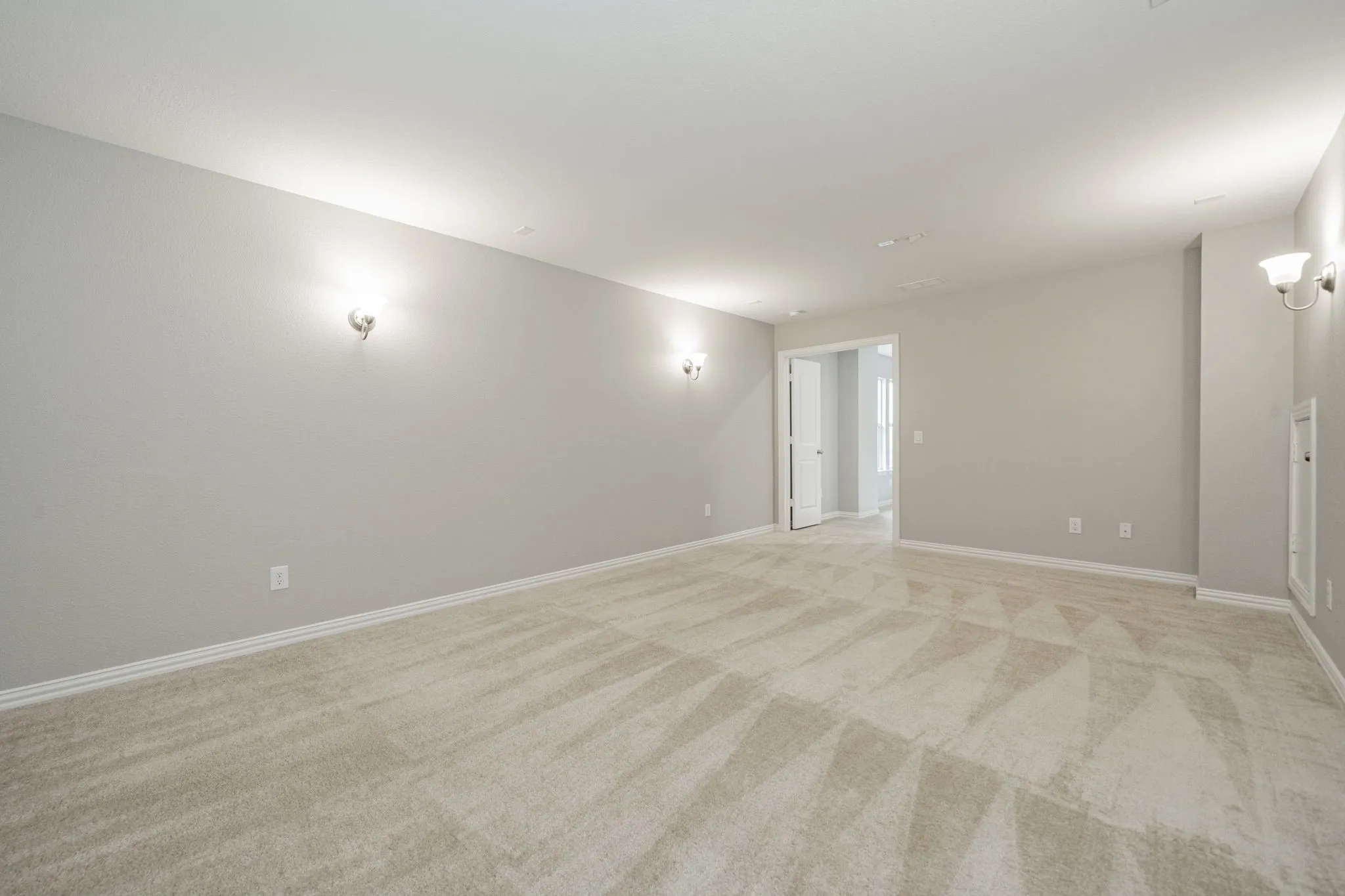 Spacious room featuring neutral carpeting, light-toned wall paint, and multiple wall-mounted sconce light fixtures