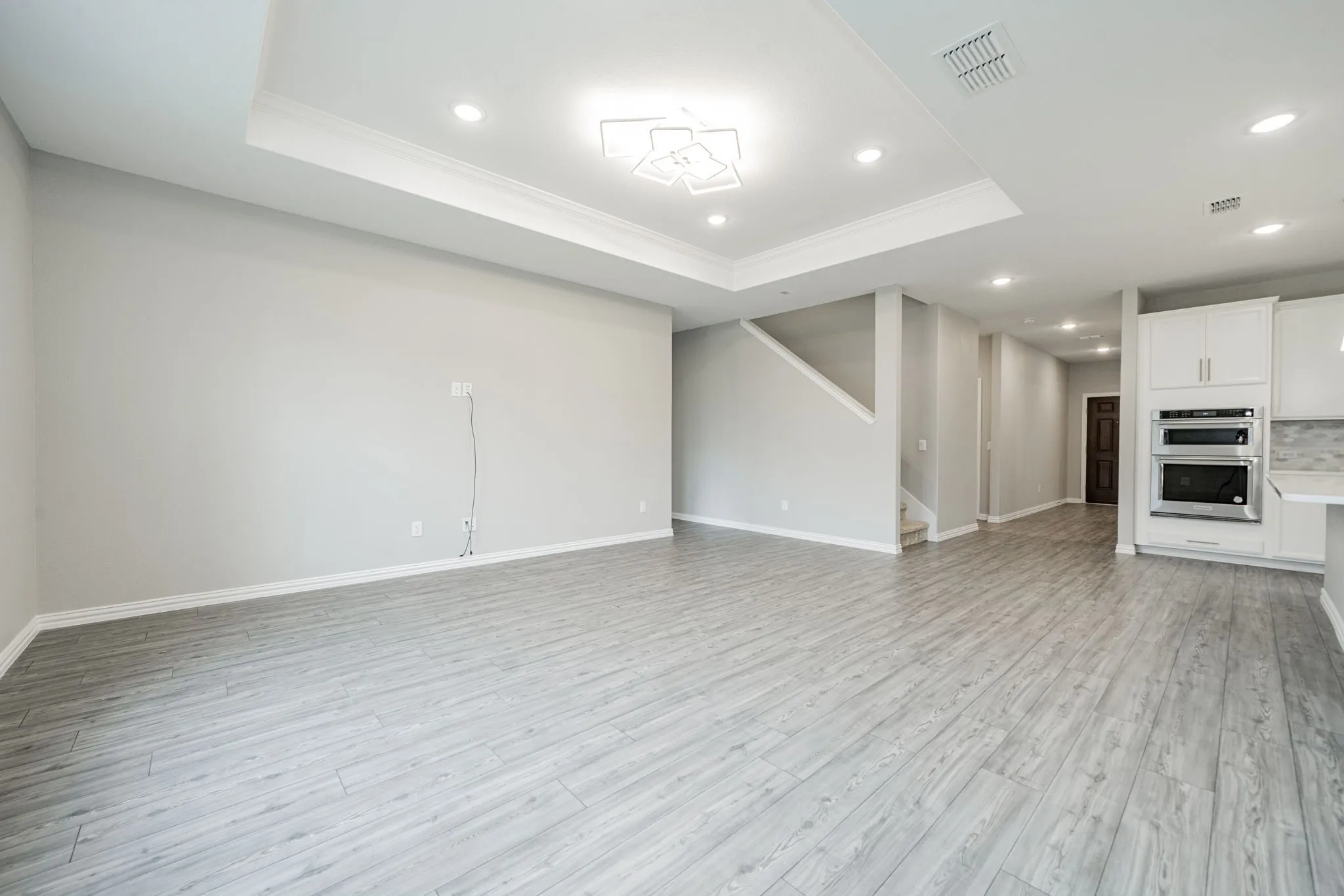 Recessed lighting, wood-finish flooring, tray ceiling, stainless steel double ovens, and white cabinetry