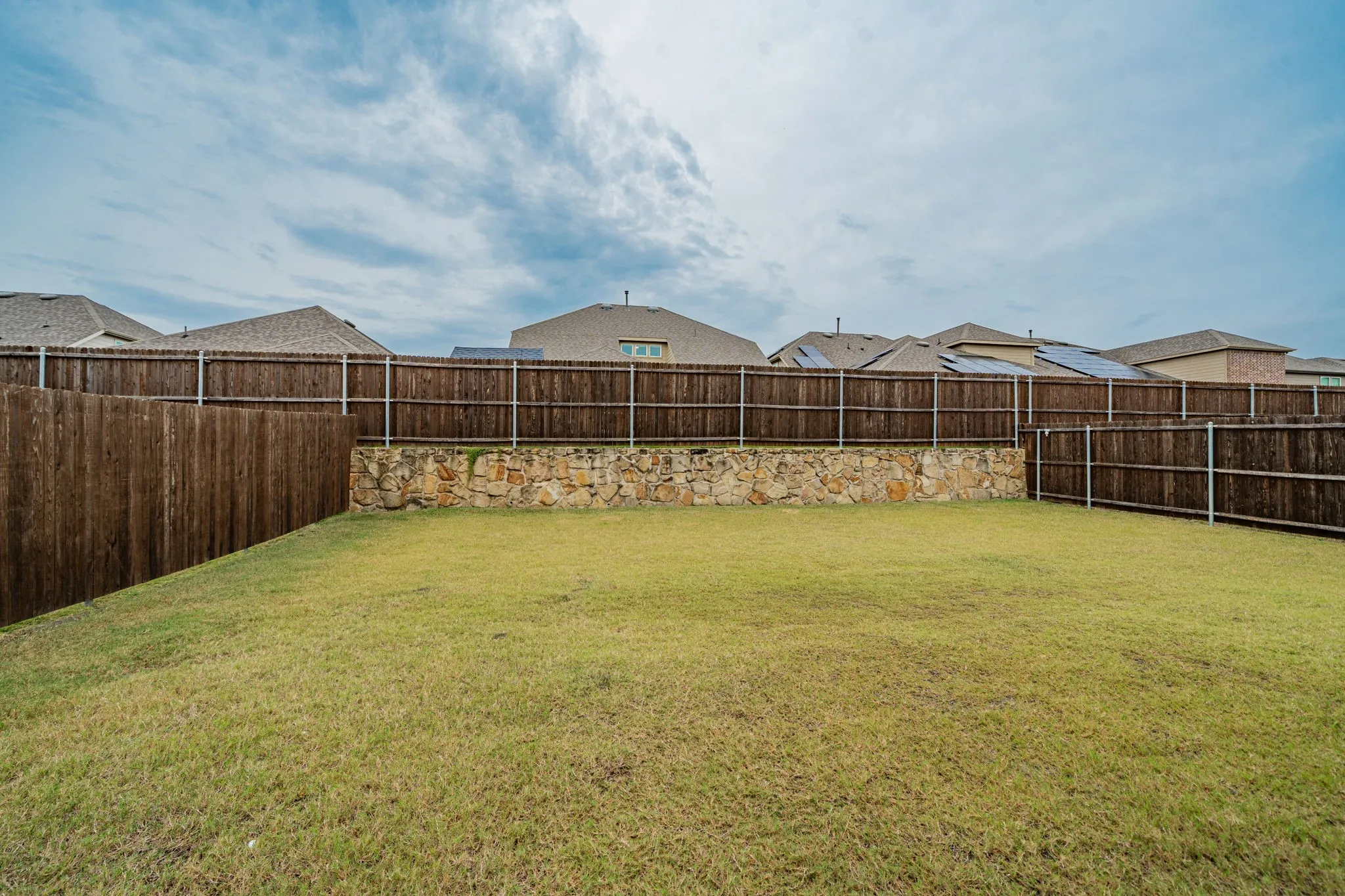 Expansive backyard featuring a manicured lawn, wood privacy fencing, and a stone retaining wall