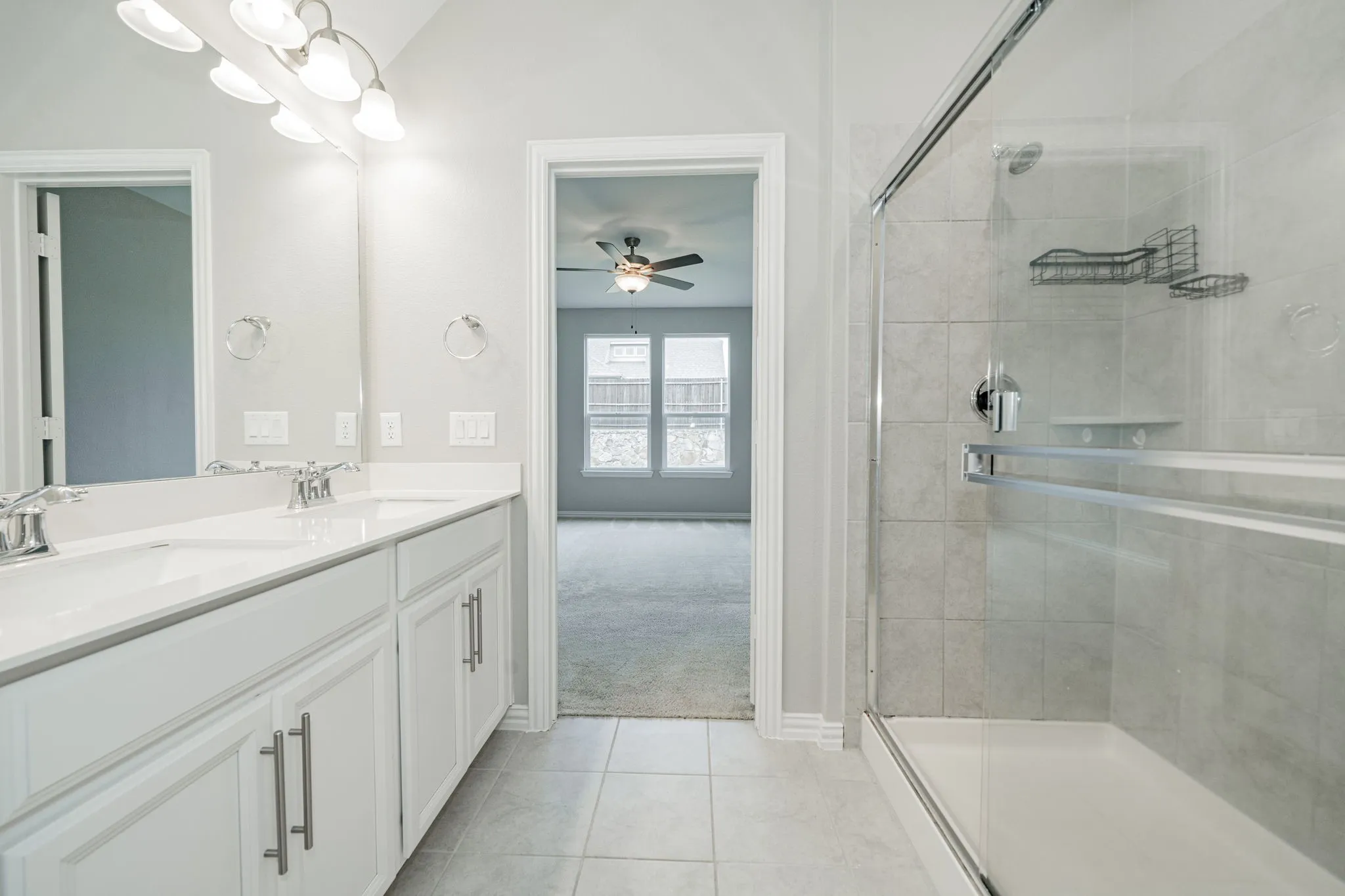 Dual vanity with white cabinetry, tile flooring, and a glass-enclosed shower