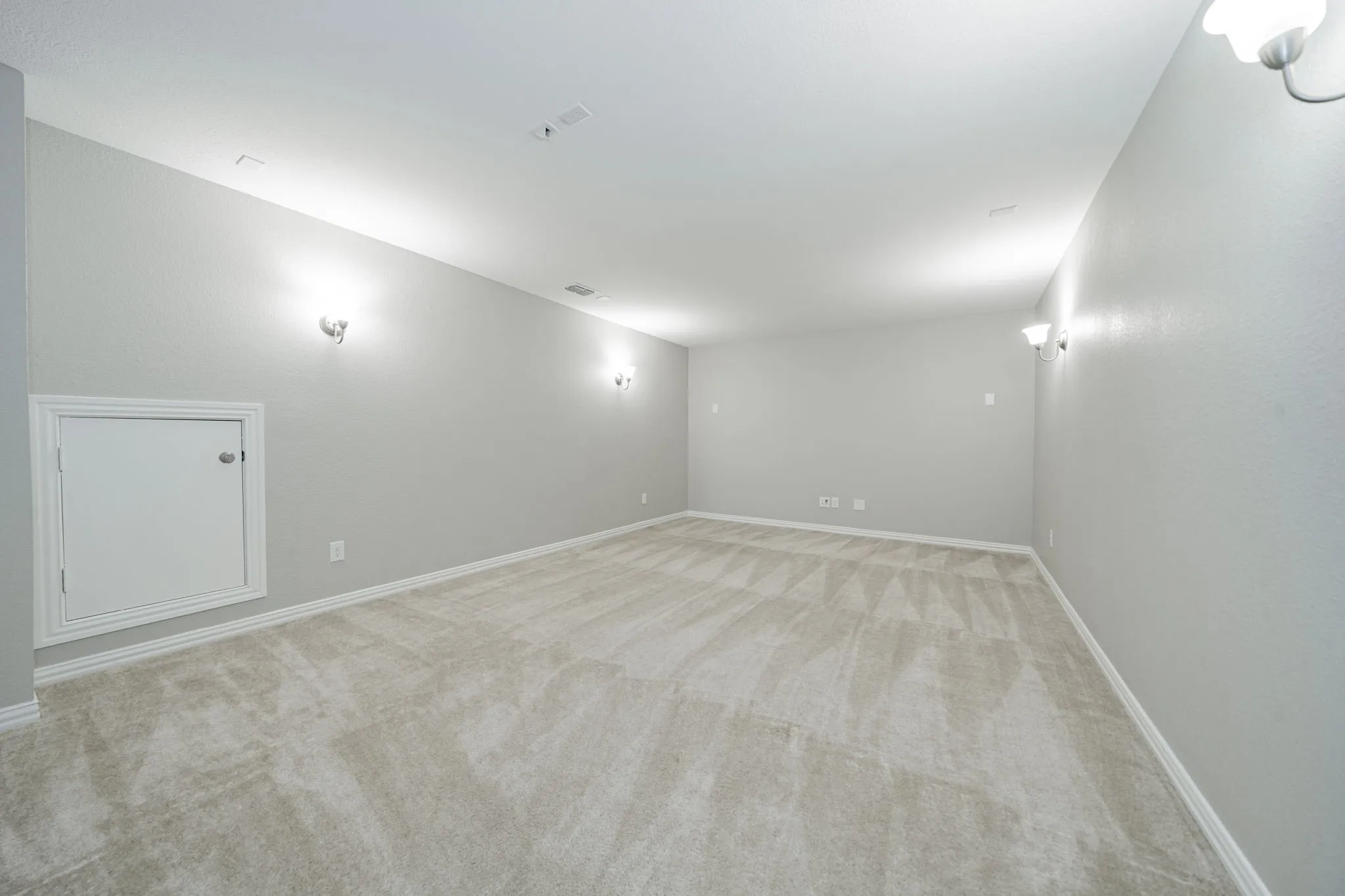 Spacious room with light-toned carpet, neutral wall paint, and multiple wall sconces