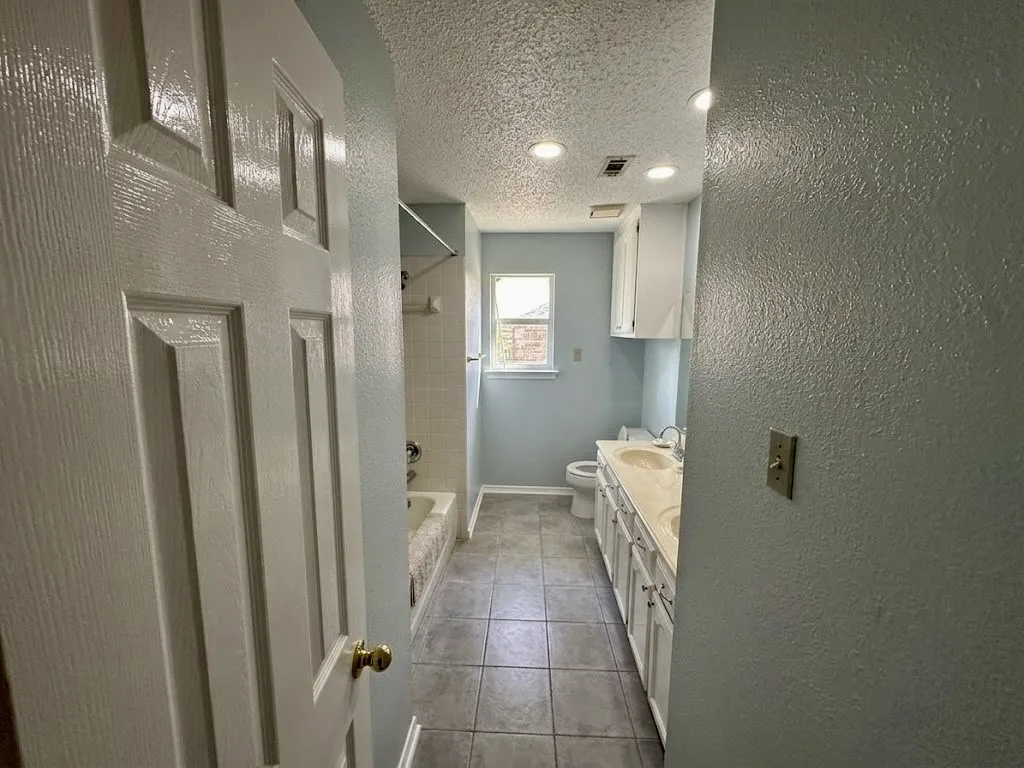 Bathroom featuring a tiled floor, dual vanity with undermount sinks, built-in cabinetry, and a bathtub with tiled surround