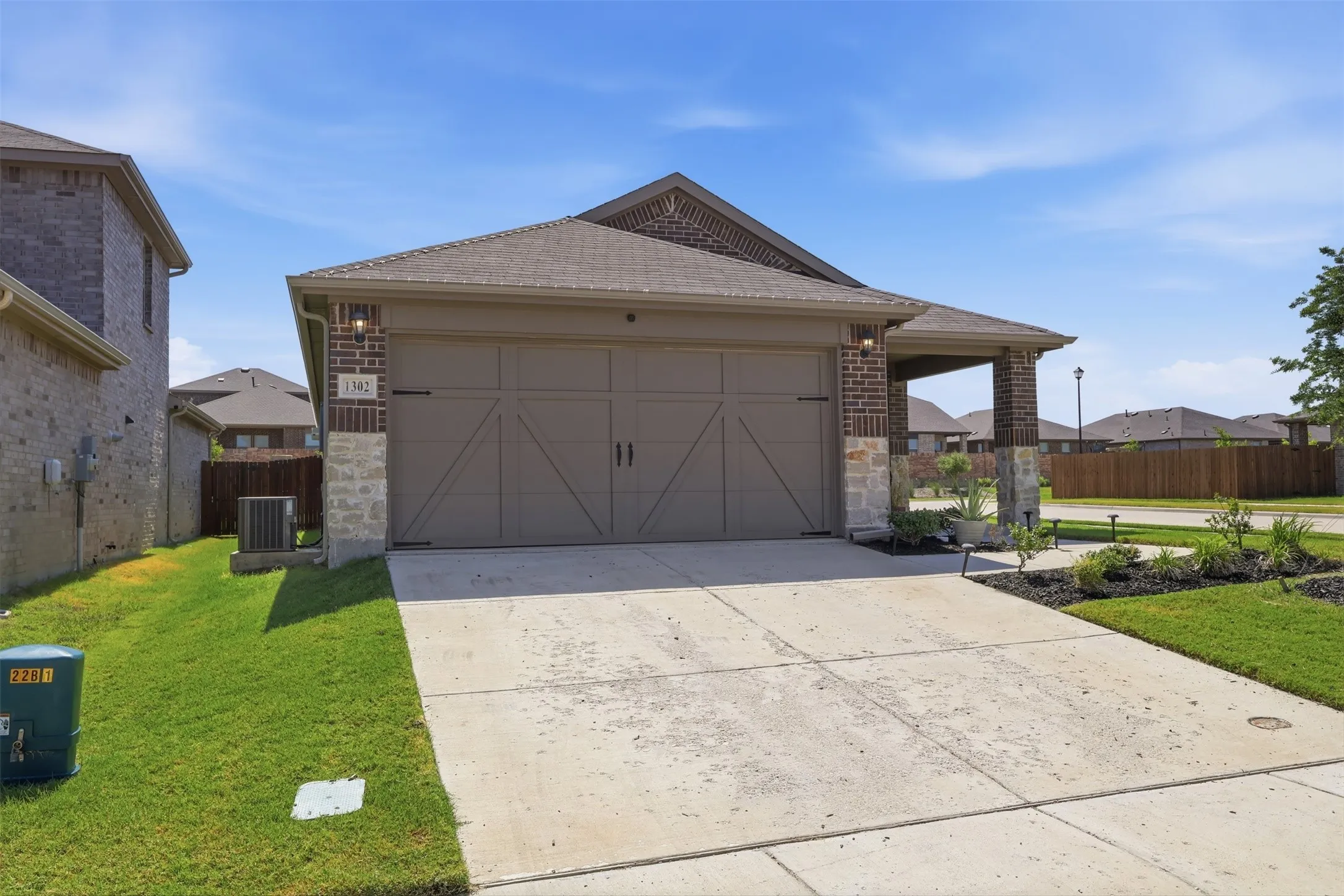 Brick and stone veneer exterior with a covered entry, two-car garage, concrete driveway, and landscaped front yard