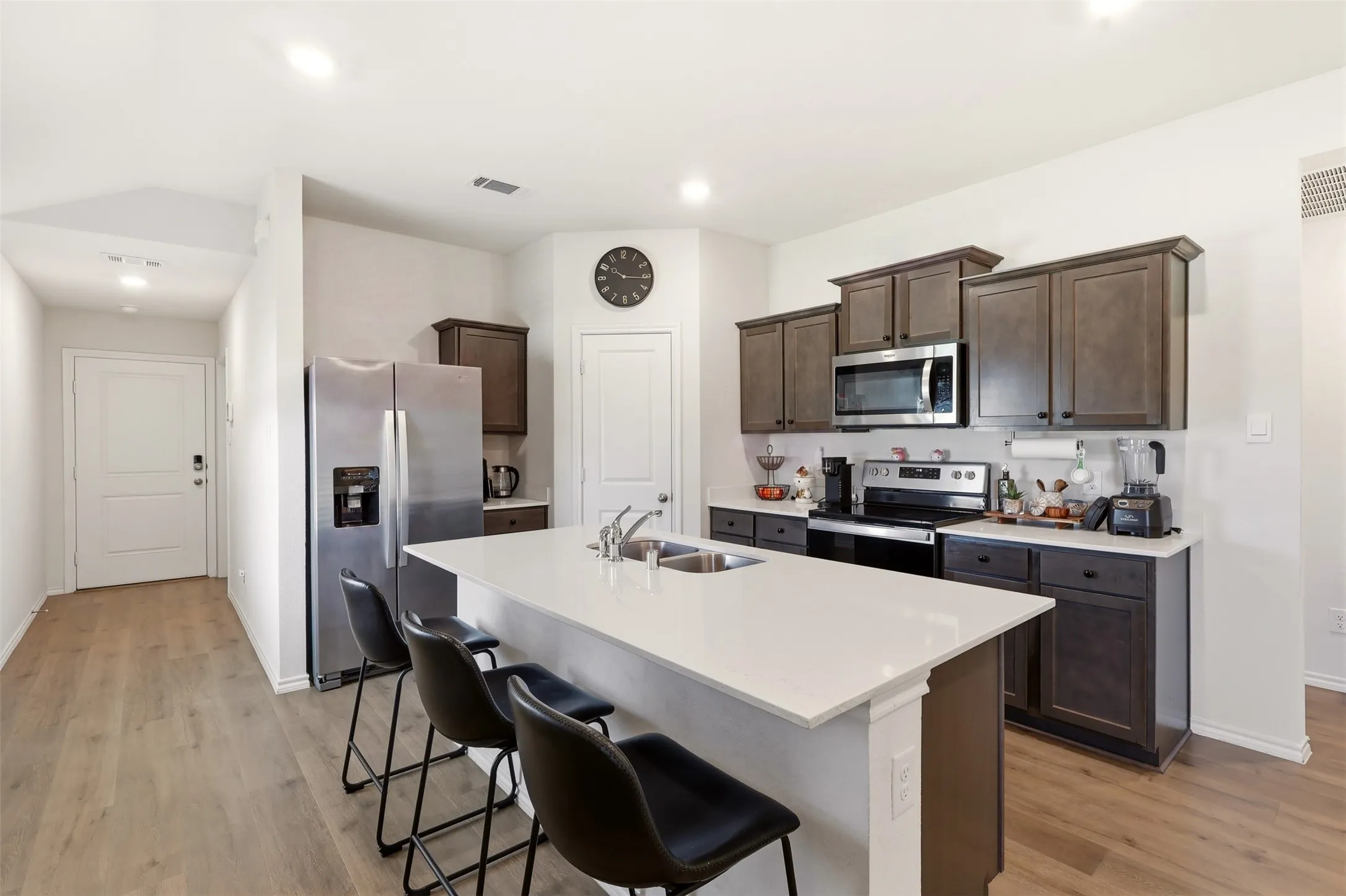 Kitchen featuring an island with a built-in sink, dark wood-finish cabinetry, stainless steel appliances, and wood-finish flooring