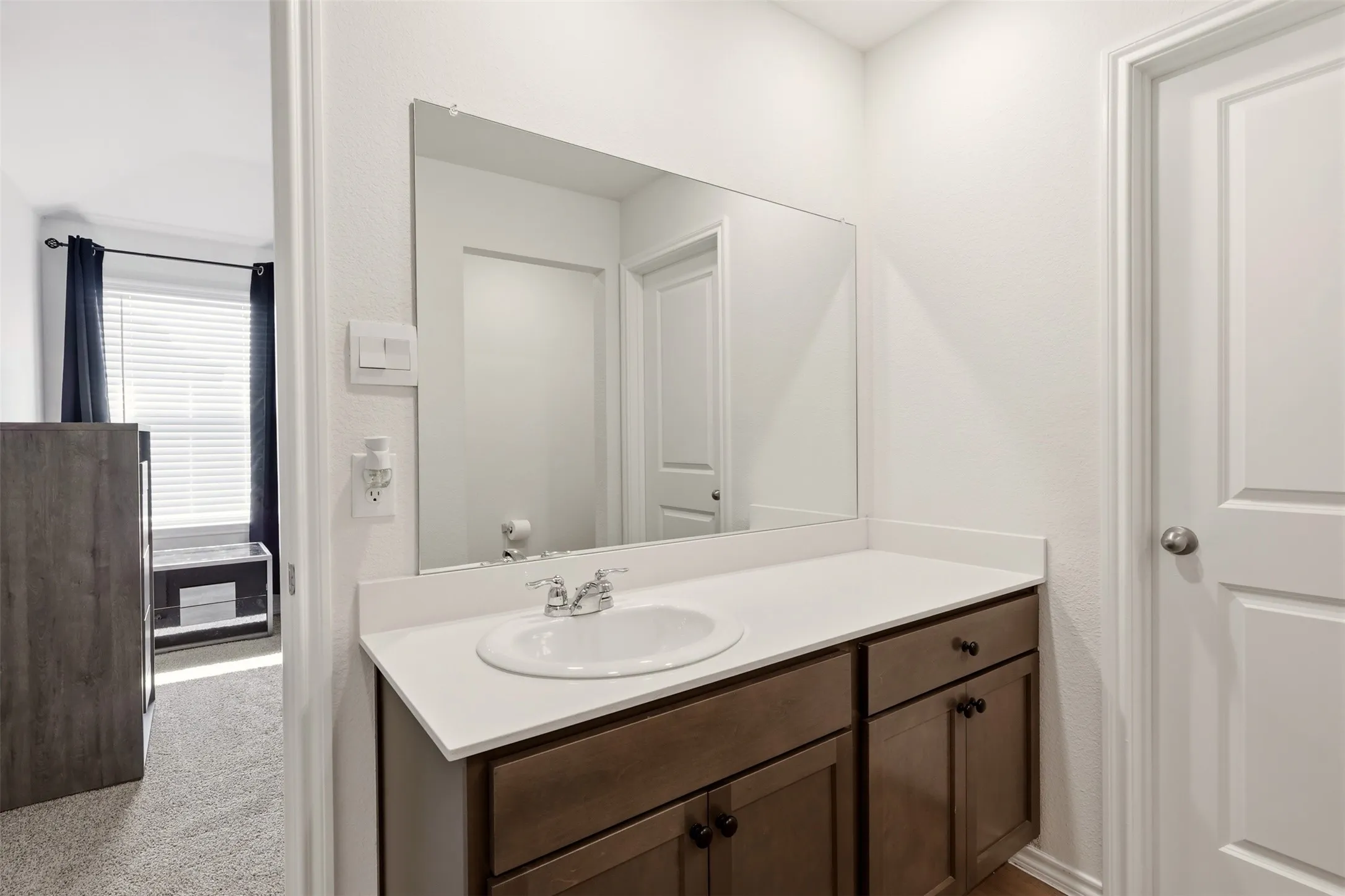 Vanity with a white countertop and integrated sink, dual-door cabinetry, a full-width mirror, and a privacy door