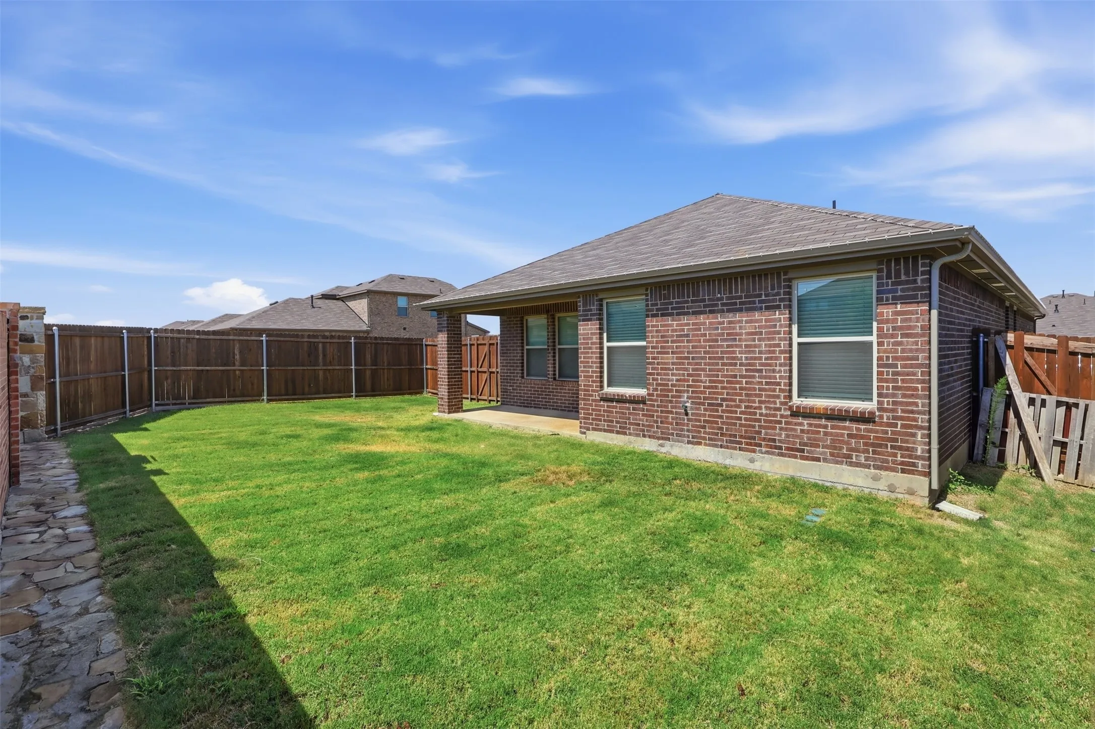 Expansive backyard featuring a manicured lawn, brick exterior, full wood privacy fence, and a covered patio