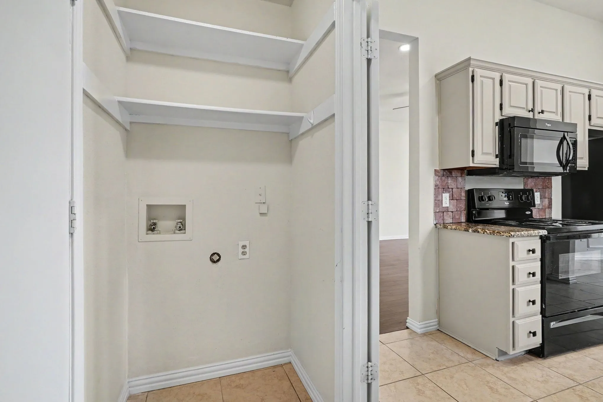 Pantry featuring open shelving with metal brackets and ample storage capacity, ceramic tile flooring, and direct access to the kitchen area with stainless steel appliances and cabinetry visible beyond