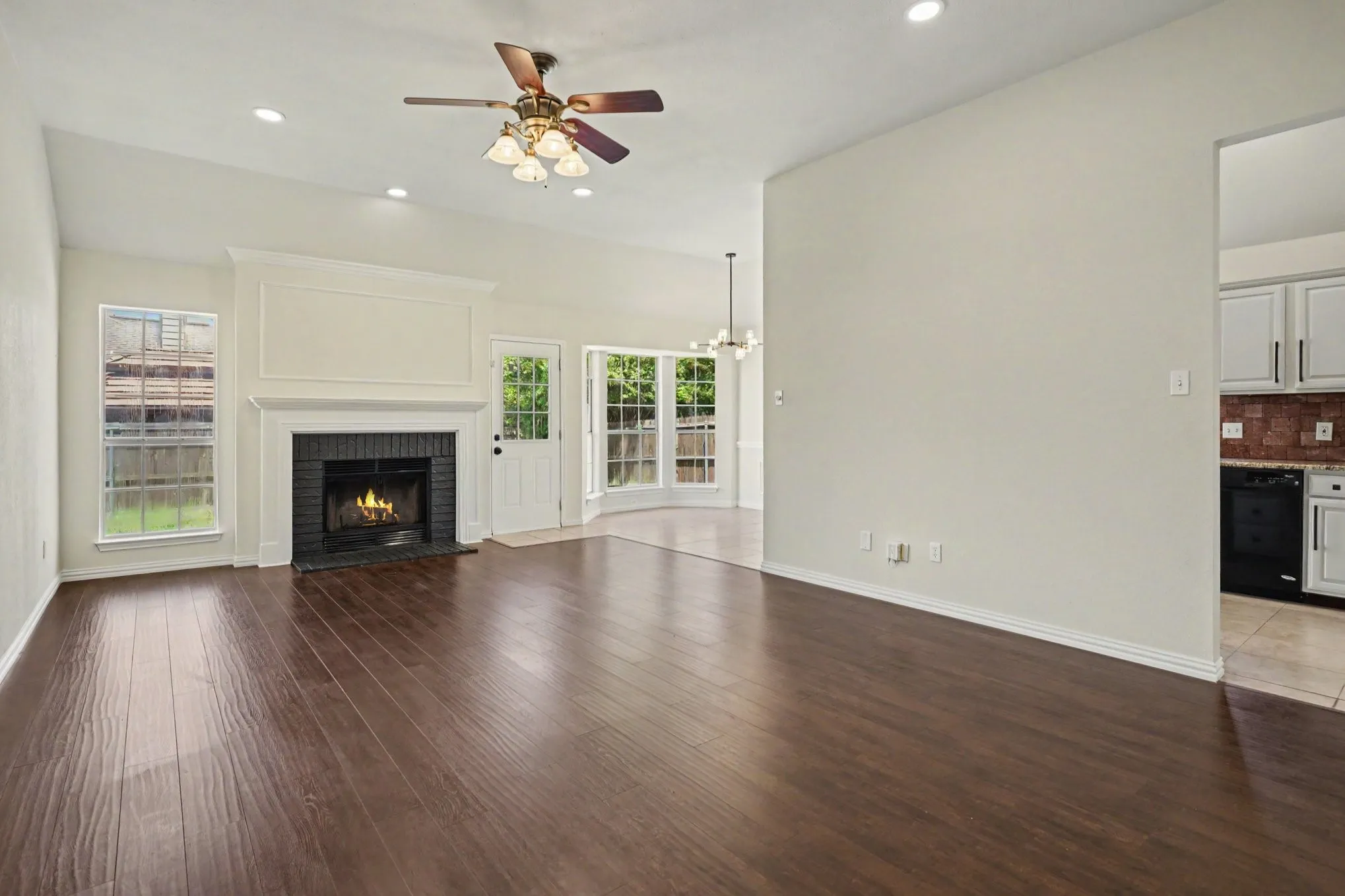 Vaulted ceiling with recessed lighting and ceiling fan, wood-finish flooring, fireplace with a black brick surround and white mantel, and an exterior door with glass panels