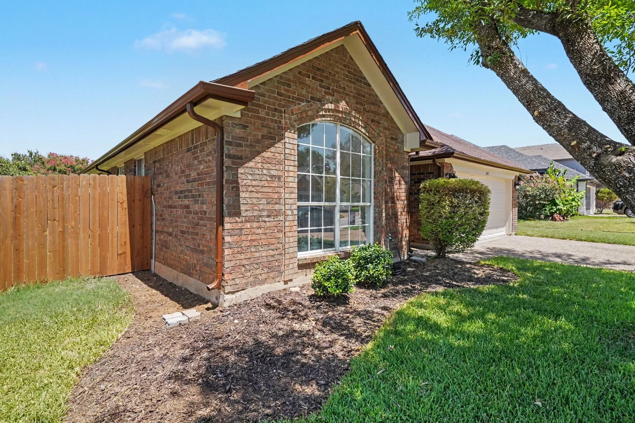 Brick exterior with an arched window, attached garage, and a wood privacy fence