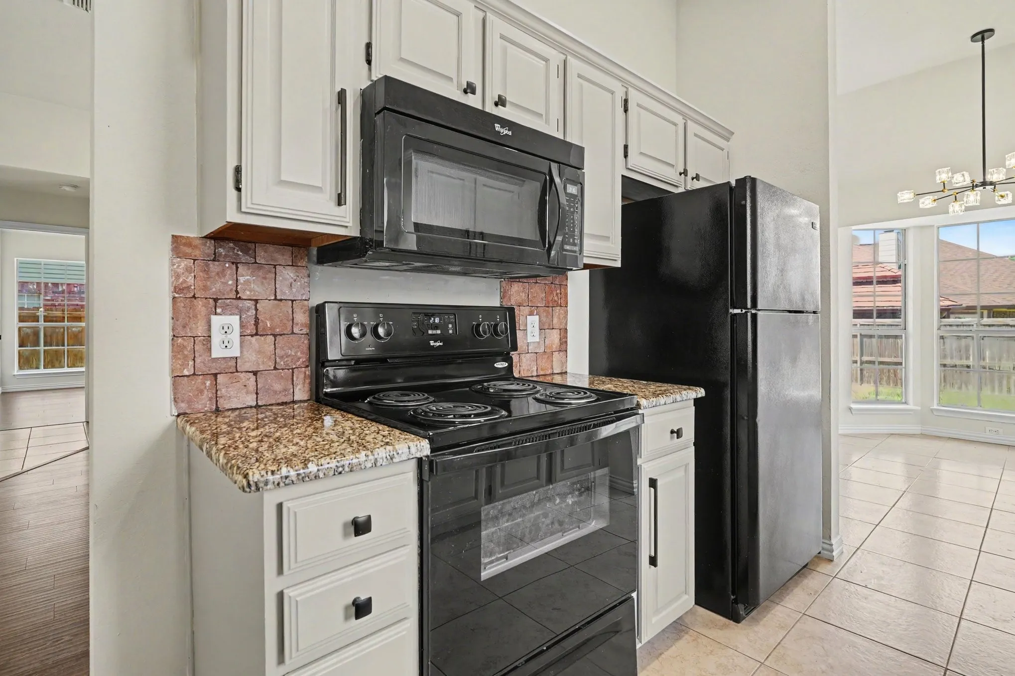 Kitchen featuring light-toned cabinetry, granite-finish countertops, and a brick-patterned backsplash