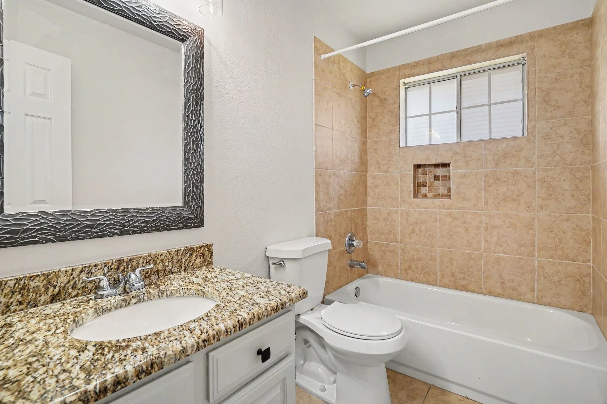 Bathroom featuring a vanity with a granite-style countertop, an undermount sink, a framed mirror, a tiled shower surround, and an integrated shower niche with mosaic tile