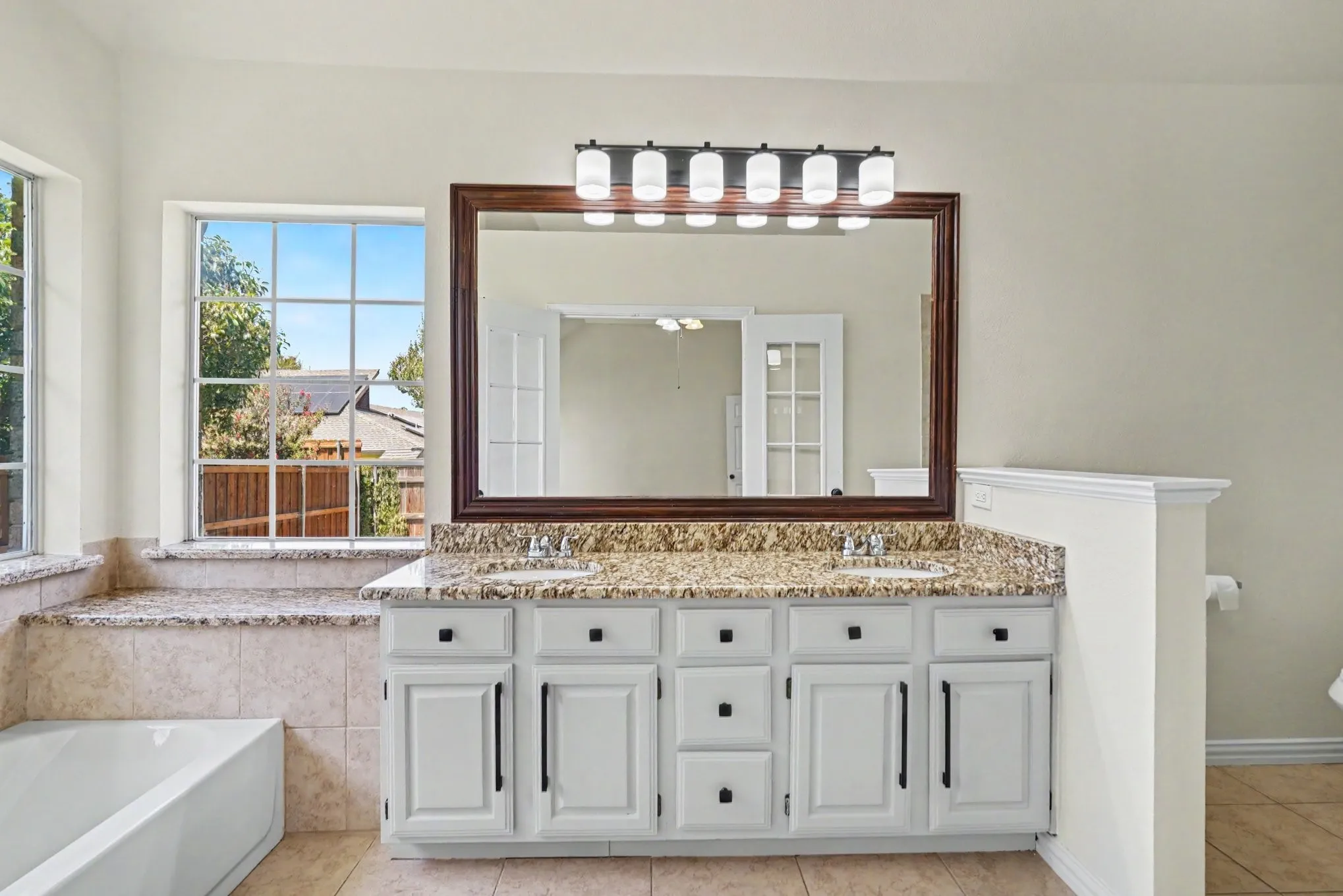 Dual vanity with a stone countertop, framed mirror, and five-light fixture