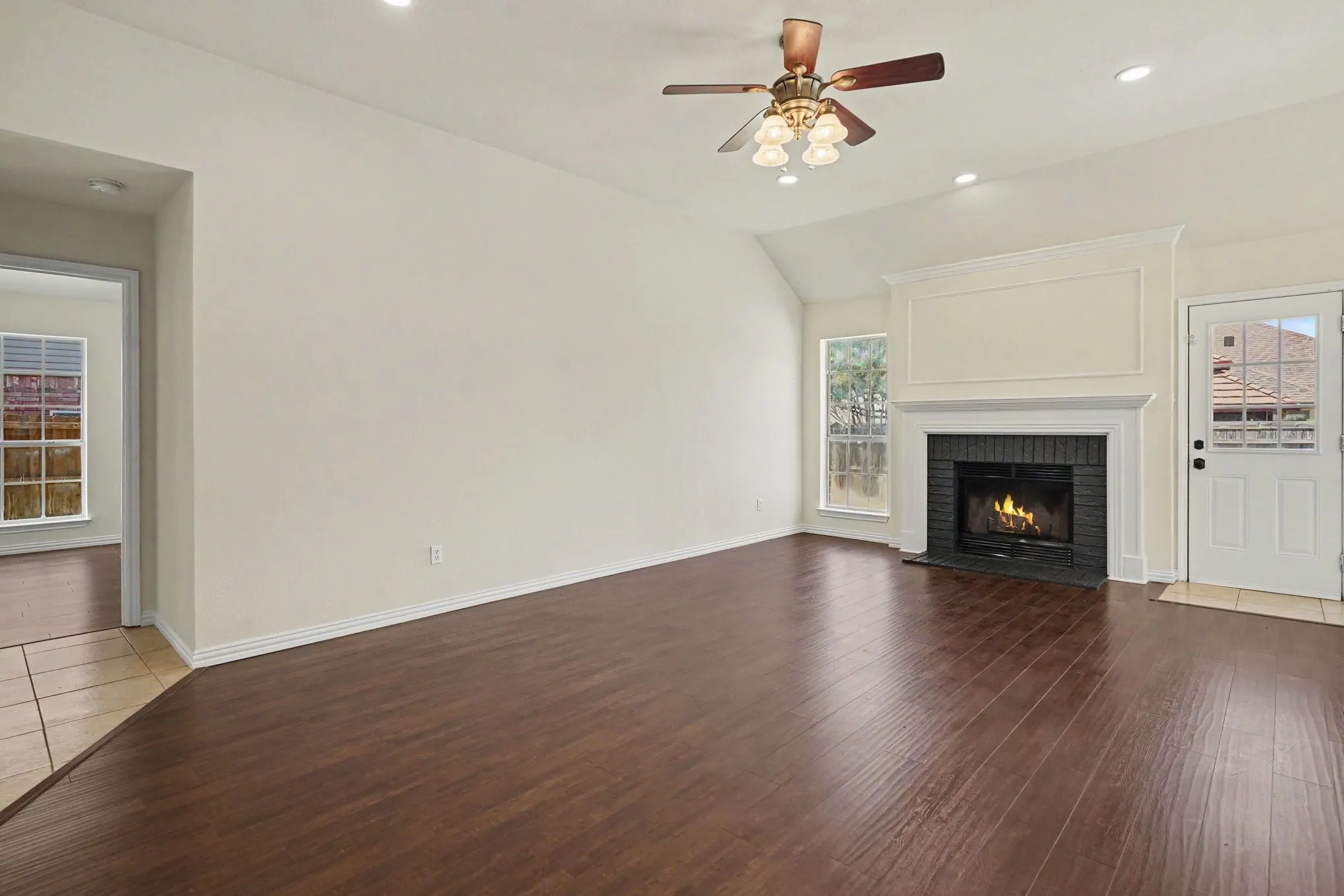 Vaulted ceiling with a ceiling fan and recessed lighting, wood-finish flooring, and a fireplace with a black brick surround and white mantel
