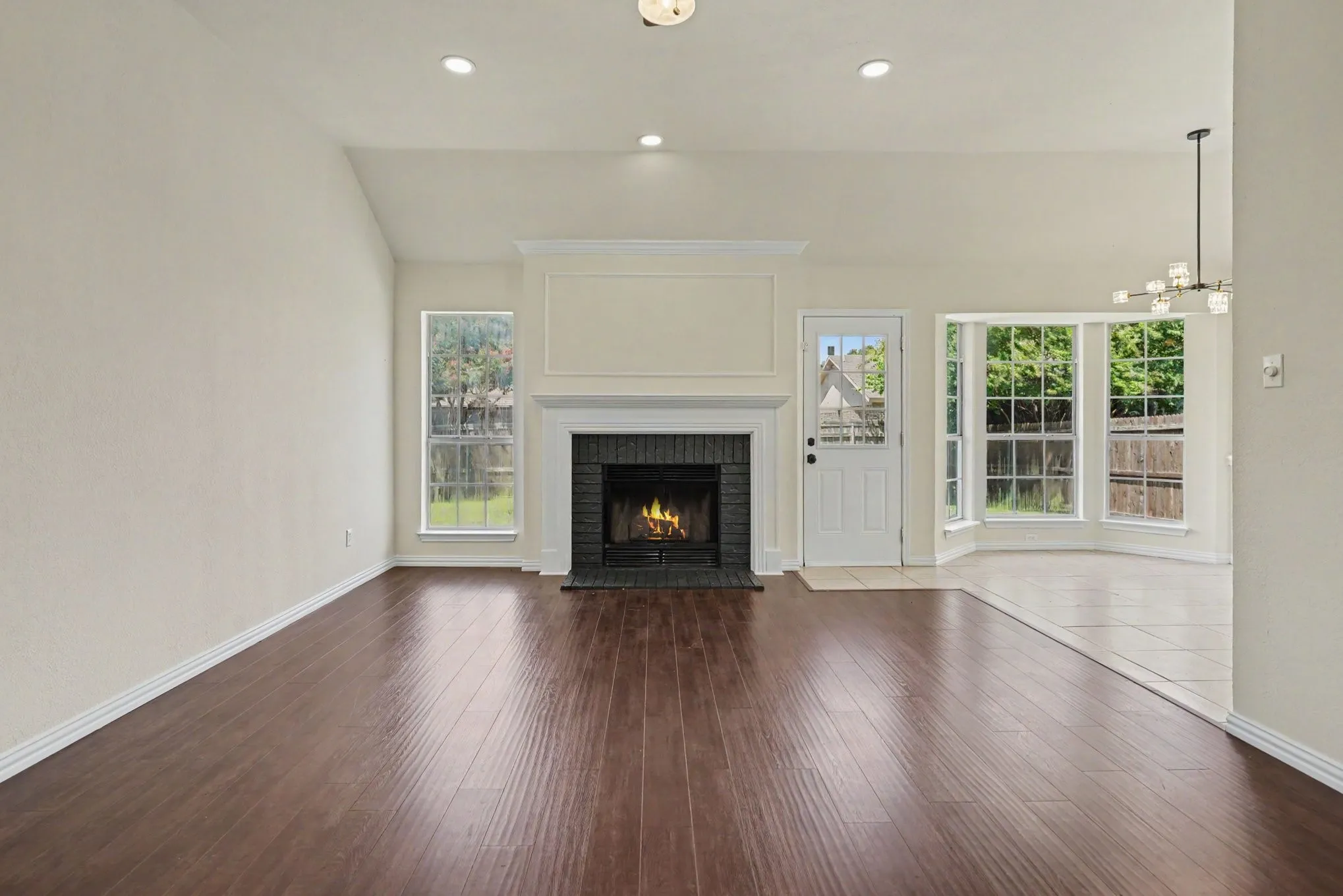 Vaulted ceiling with recessed lighting, wood-finish flooring, brick fireplace with white mantel, bay window, and exterior-facing door with glass paneling