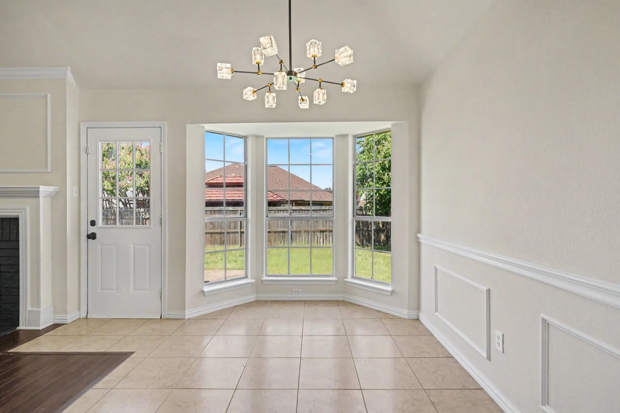 Bay window with multiple panes, modern chandelier, tile flooring, and decorative wainscoting