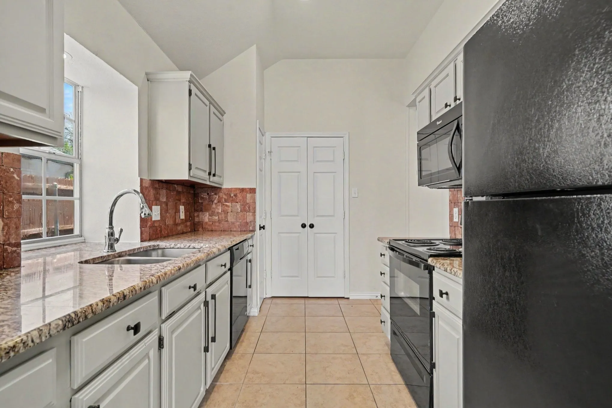 Galley kitchen featuring light-colored cabinetry, stone countertops, a tile backsplash, and a stainless steel sink with a gooseneck faucet