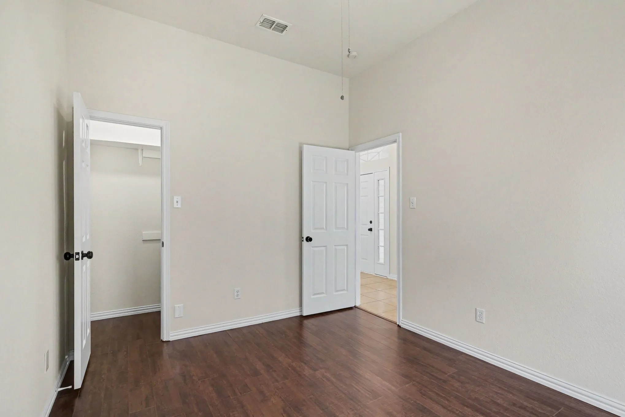 Spacious room featuring rich wood-finish flooring, pristine white walls, and multiple entry points including two six-panel doors