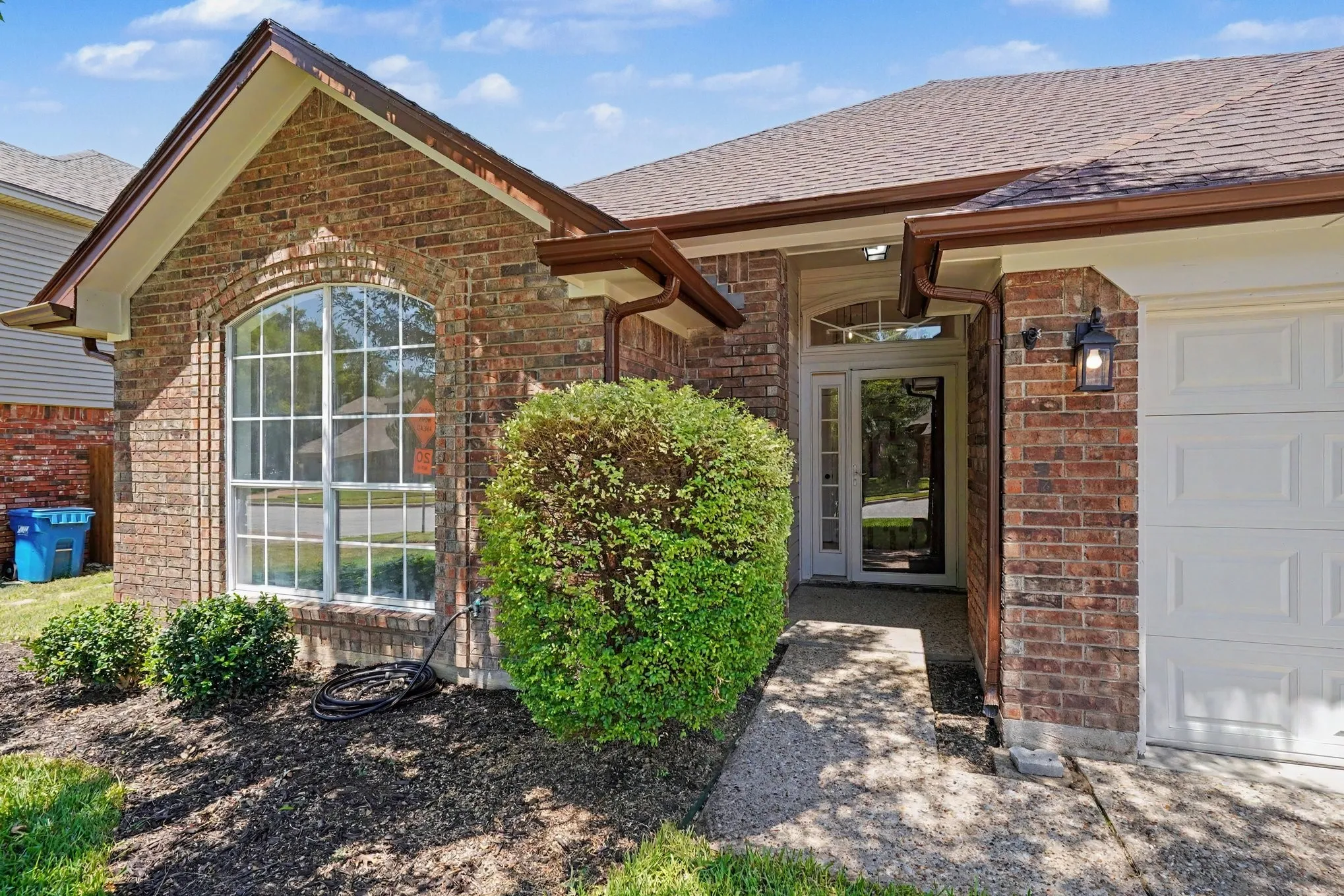 Brick exterior with architectural arched window, covered entryway, attached garage, and landscaping