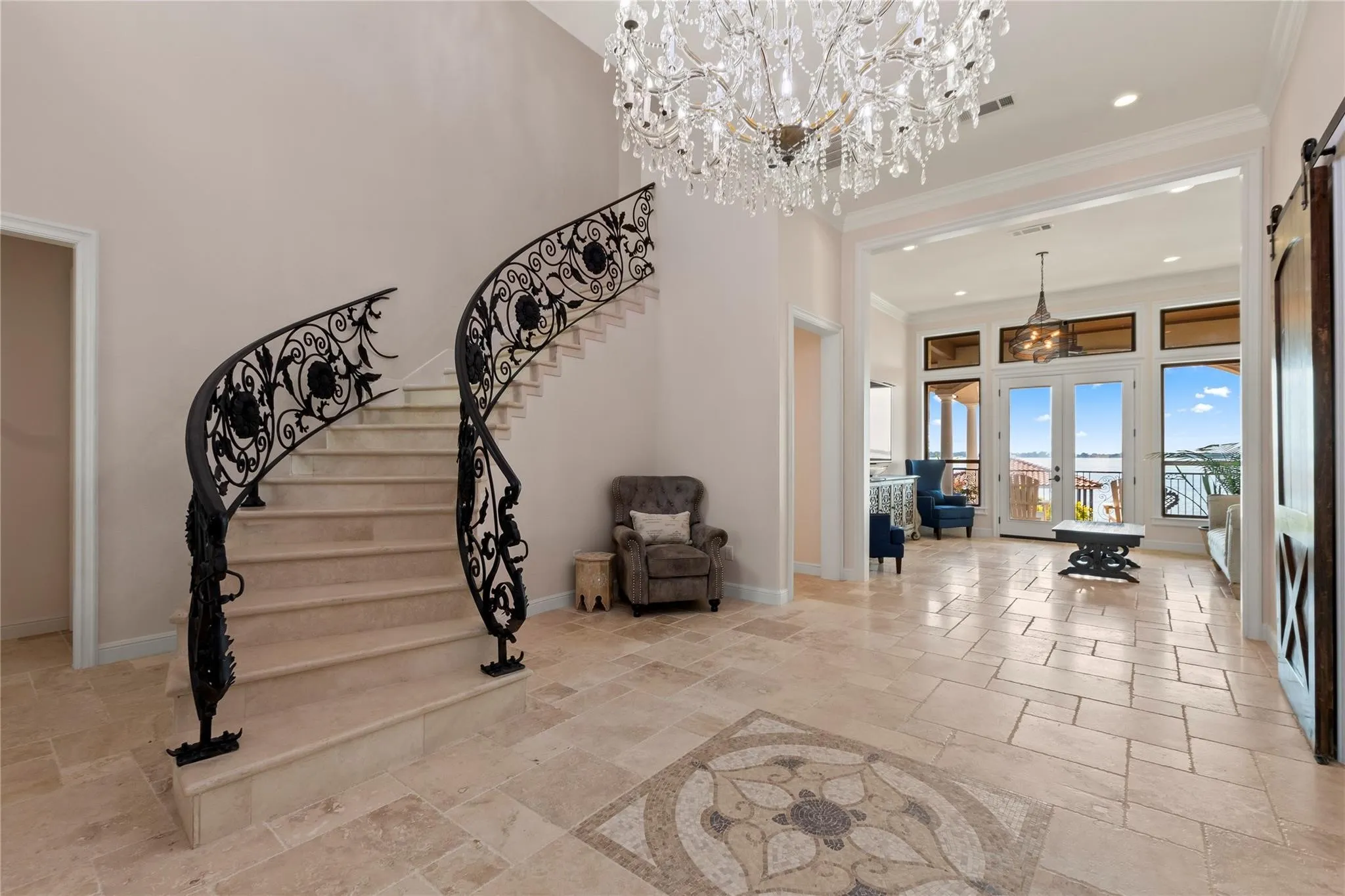 Stunning entry featuring chandeliers, elegant winding staircase, inlaid tile and welcoming water views