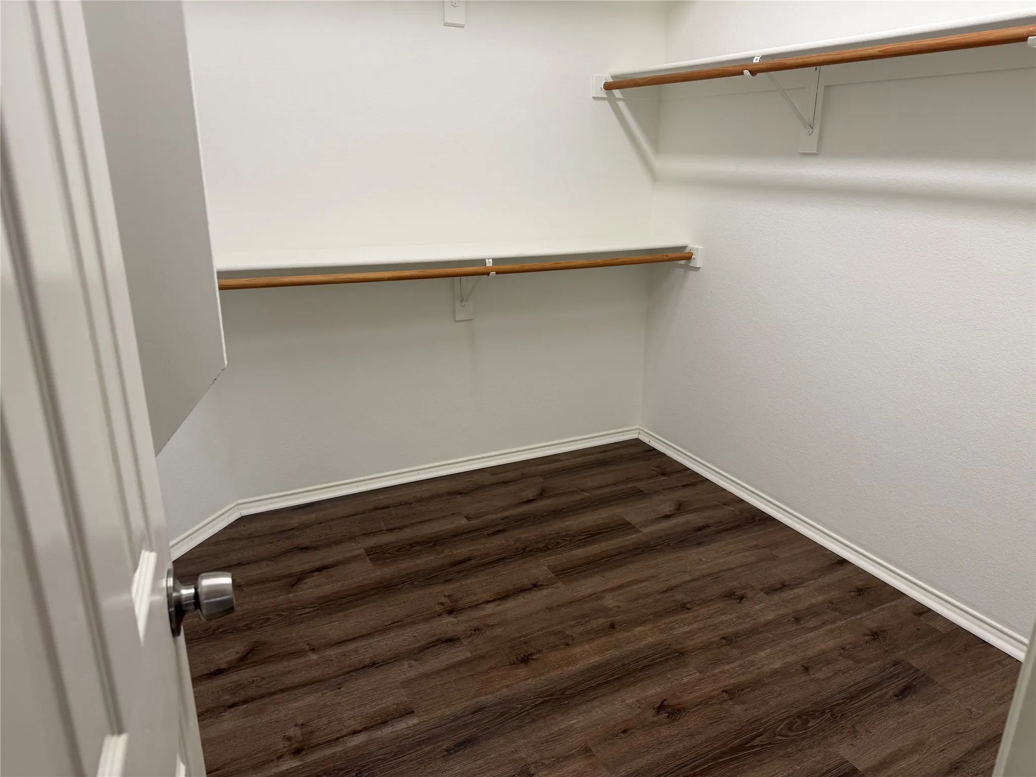 Walk-in closet with wood-finish flooring, white walls, and built-in shelving with hanging rods