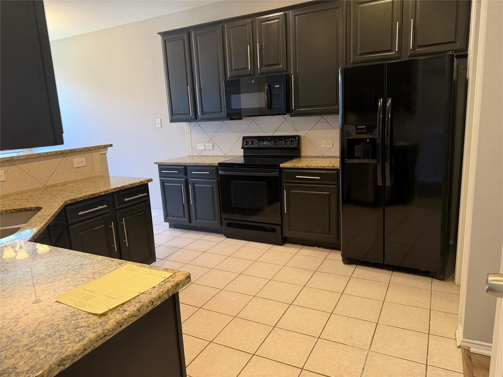 Sophisticated kitchen featuring black cabinetry with brushed metal hardware, granite countertops, and stainless steel appliances including a built-in microwave and range