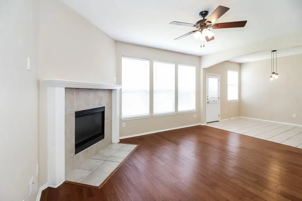 Living area featuring a fireplace with a tile surround, multiple windows, wood-finish flooring, and a ceiling fan