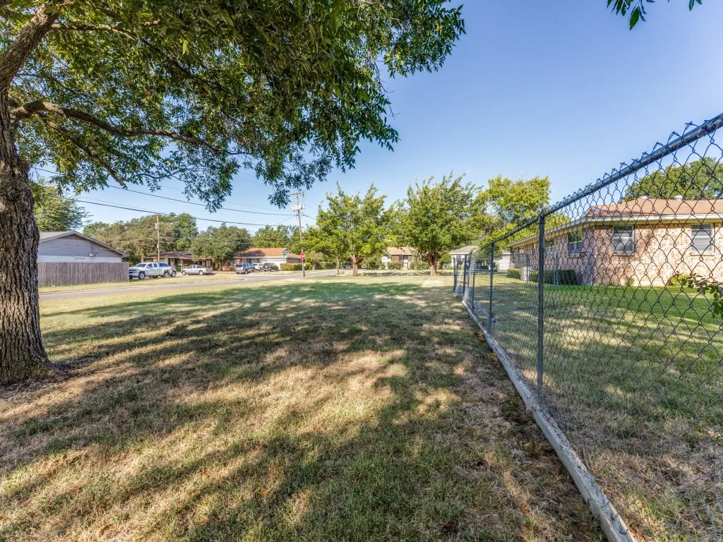 Expansive outdoor space featuring a chain-link fence, a mature tree, and surrounding residential properties