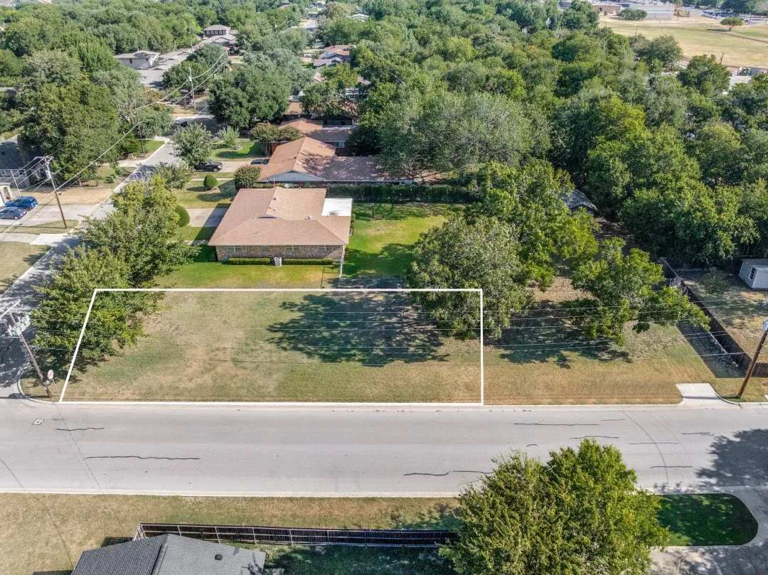 Expansive undeveloped lot with street frontage, featuring established trees and a defined boundary