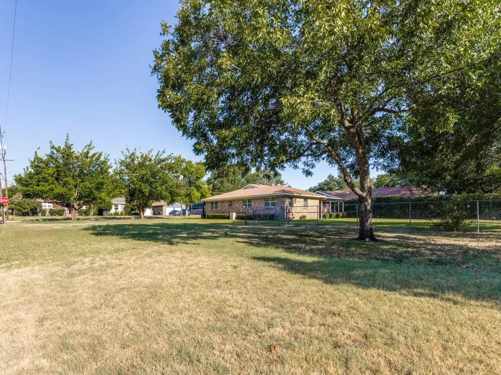 Brick exterior residence with mature trees and a chain-link fence