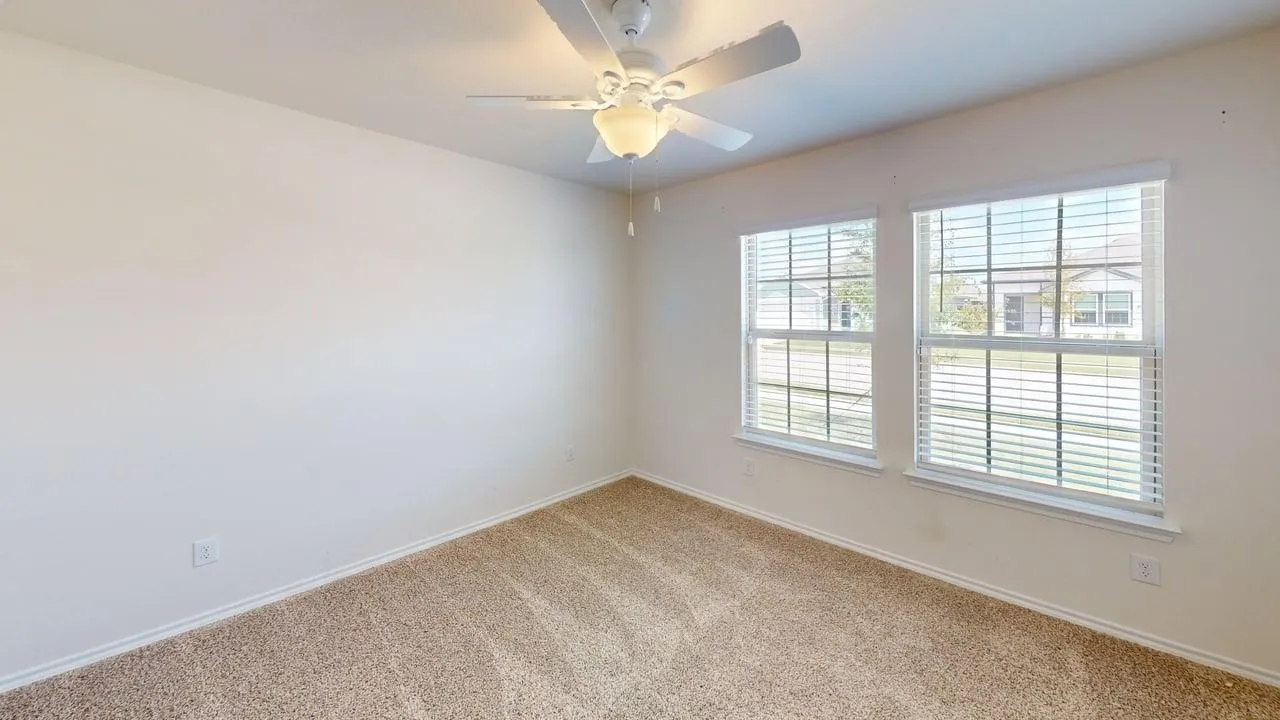Carpeted room featuring two double-hung windows with blinds, a ceiling fan with light, and neutral wall paint