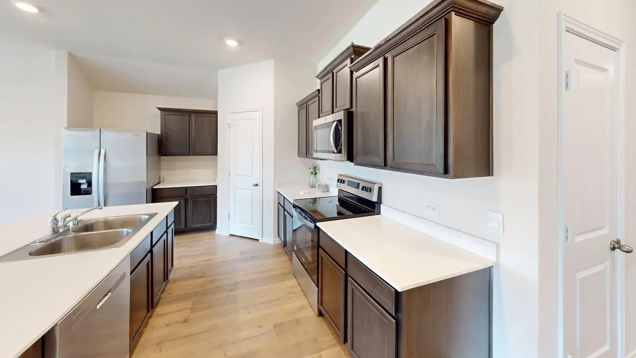Modern galley kitchen featuring stainless steel appliances, white quartz countertops, dark cabinetry with ample storage, wood-finish flooring, and an island with additional counter space