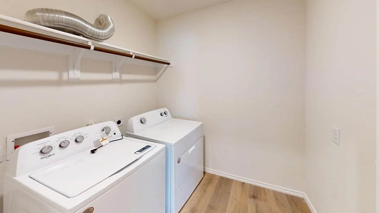 Laundry area featuring wood-finish flooring, white walls, and a built-in shelf with a hanging rod