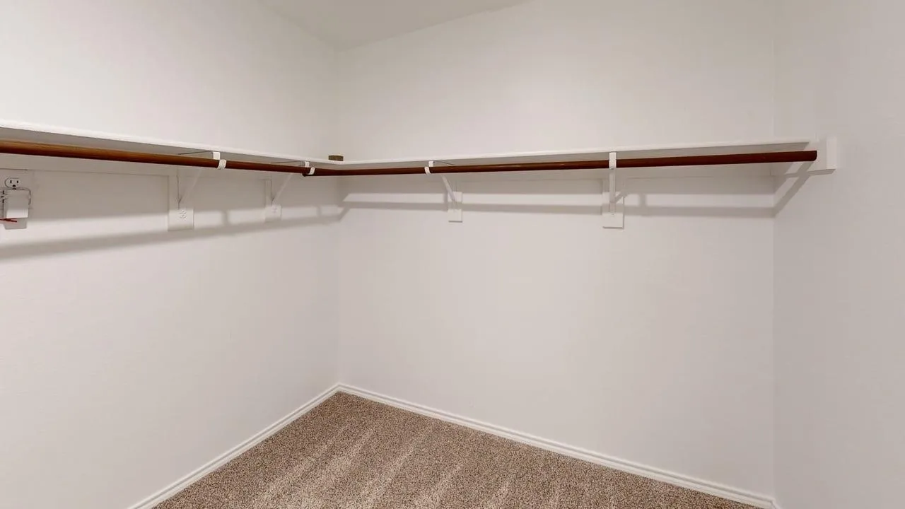 Corner built-in shelving with hanging rod, light-colored walls, and textured carpet flooring