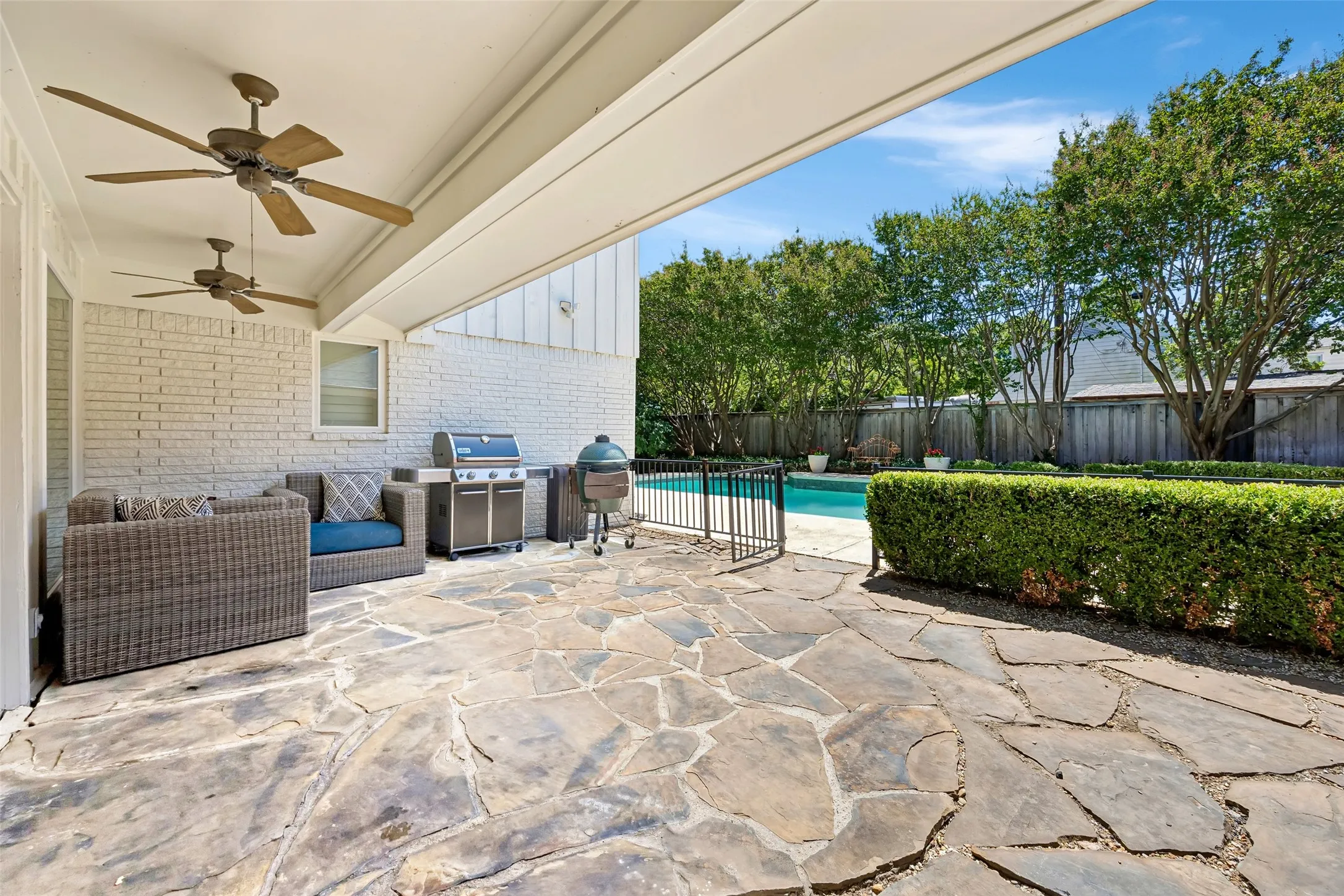 A covered flagstone patio with ceiling fans overlooks the pool and landscaped backyard, creating an inviting space for outdoor living and entertaining.