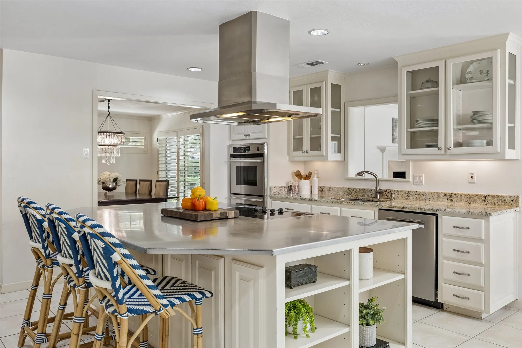 A closer view of the kitchen highlights the oversized island with seating, generous storage, glass-front cabinetry, and sleek stainless steel vent hood.